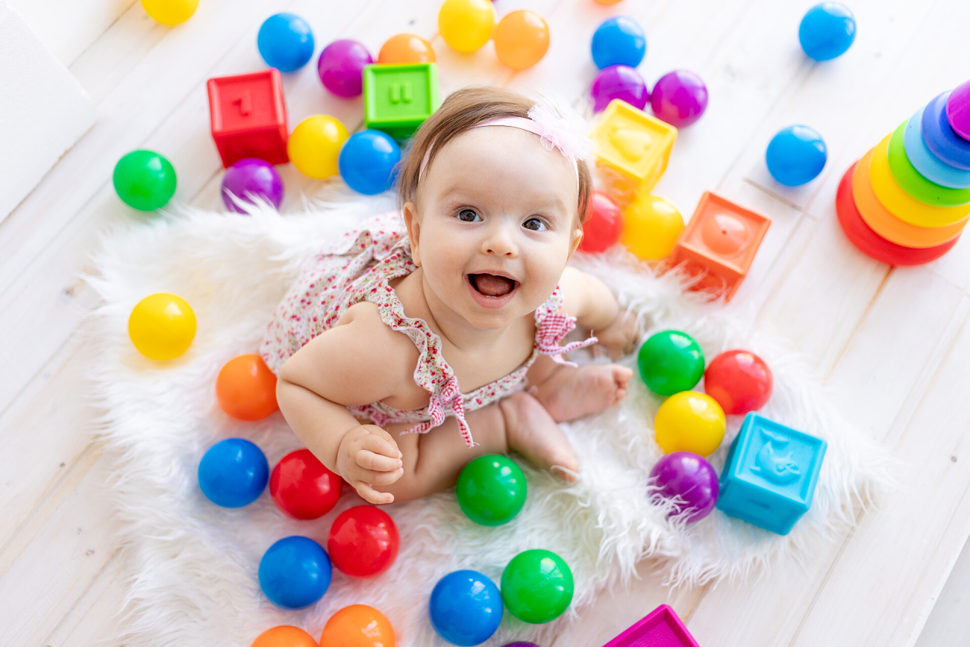 镜头下一个可爱的小宝宝？快乐的小女孩穿着一件红色的连衣裙，头戴鲜艳的玩具，坐在一个白色的房间里，望着上面