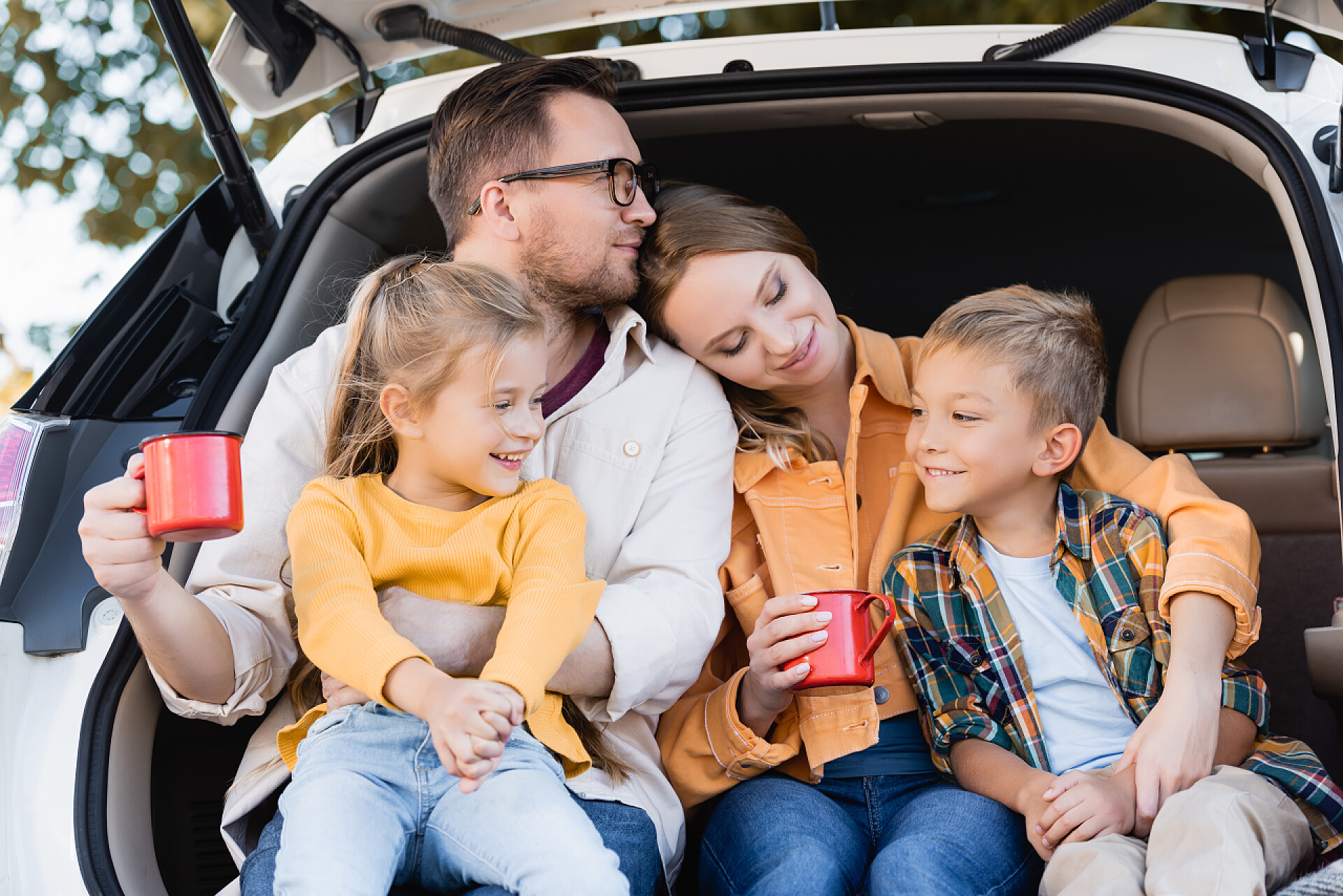 坐在后备箱里的一家四口女人在小孩身边举杯，丈夫在后备箱里 