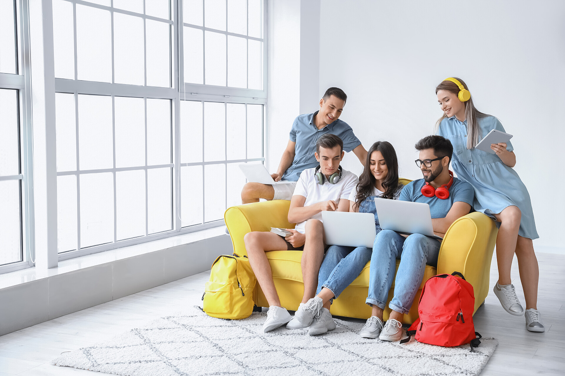 坐在沙发上学习的五个年轻人拥有现代装置的学生在室内在线学习