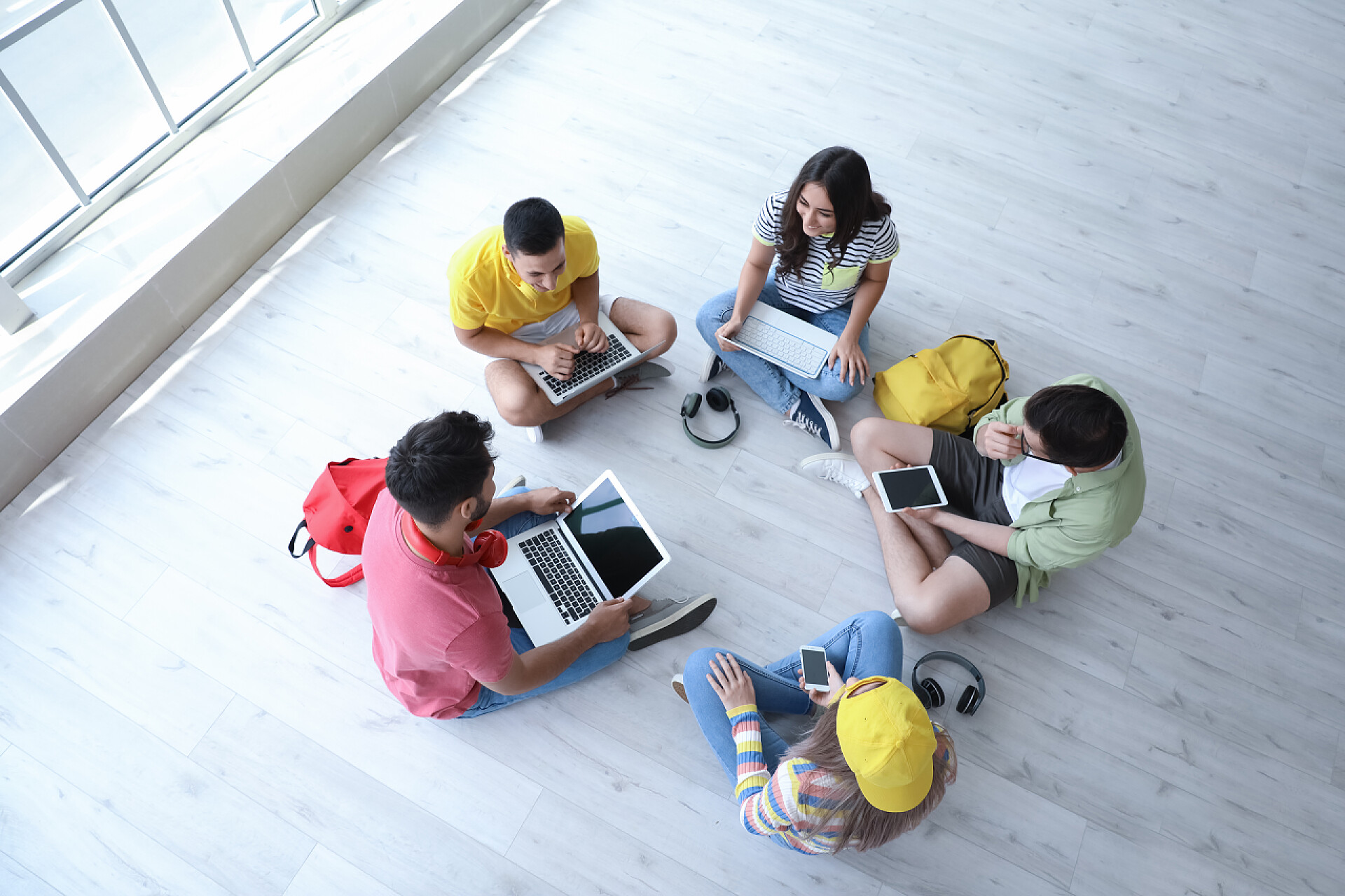五个年轻的人坐在地上学习拥有现代装置的学生在室内在线学习