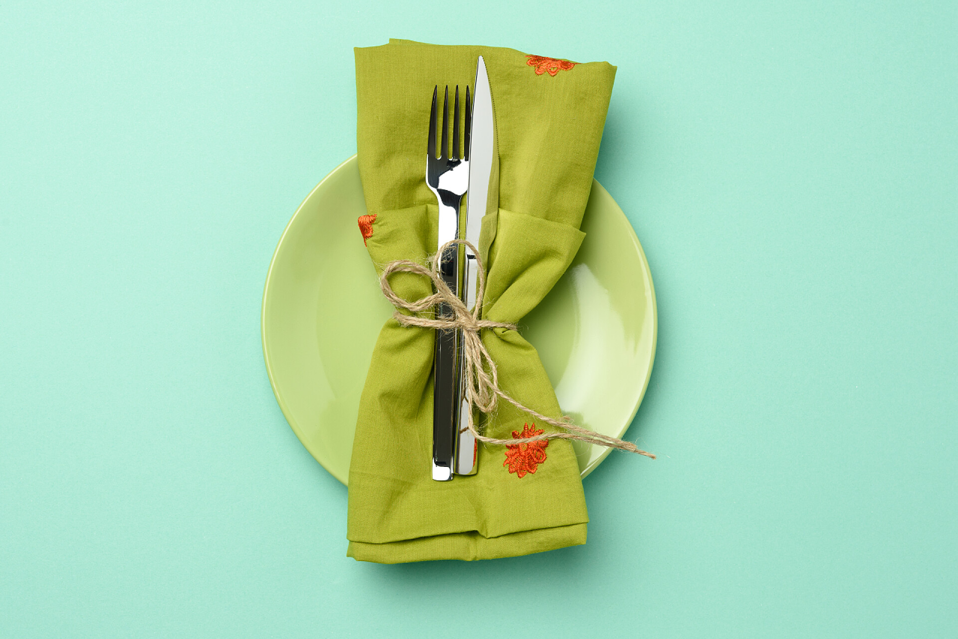 绿色背景下绿色盘子里的绿布空圆形绿色陶瓷板和金属叉和刀，绿色背景，顶部视图