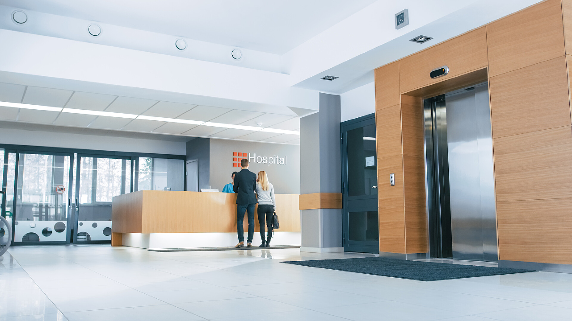 医院的前台与前台进行沟通的夫妻在医院大厅里，年轻夫妇与接待员交谈。新的现代医疗设施.