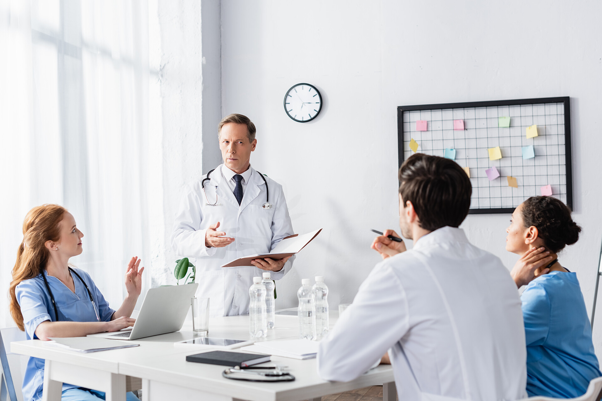 四个讨论的医生在诊所使用笔记本电脑和纸质文件夹的多族裔医院工作人员 