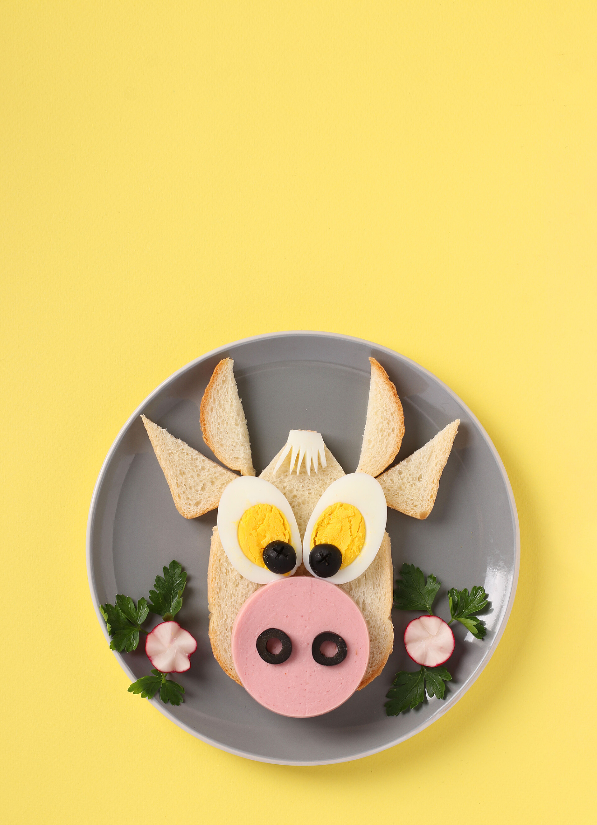 黄色桌子上的灰色盘子和公牛面包夹杂着香肠和鸡蛋的三明治形状有趣的公牛，象征2021年的新的黄色背景，为孩子们做饭的想法。纵向格式