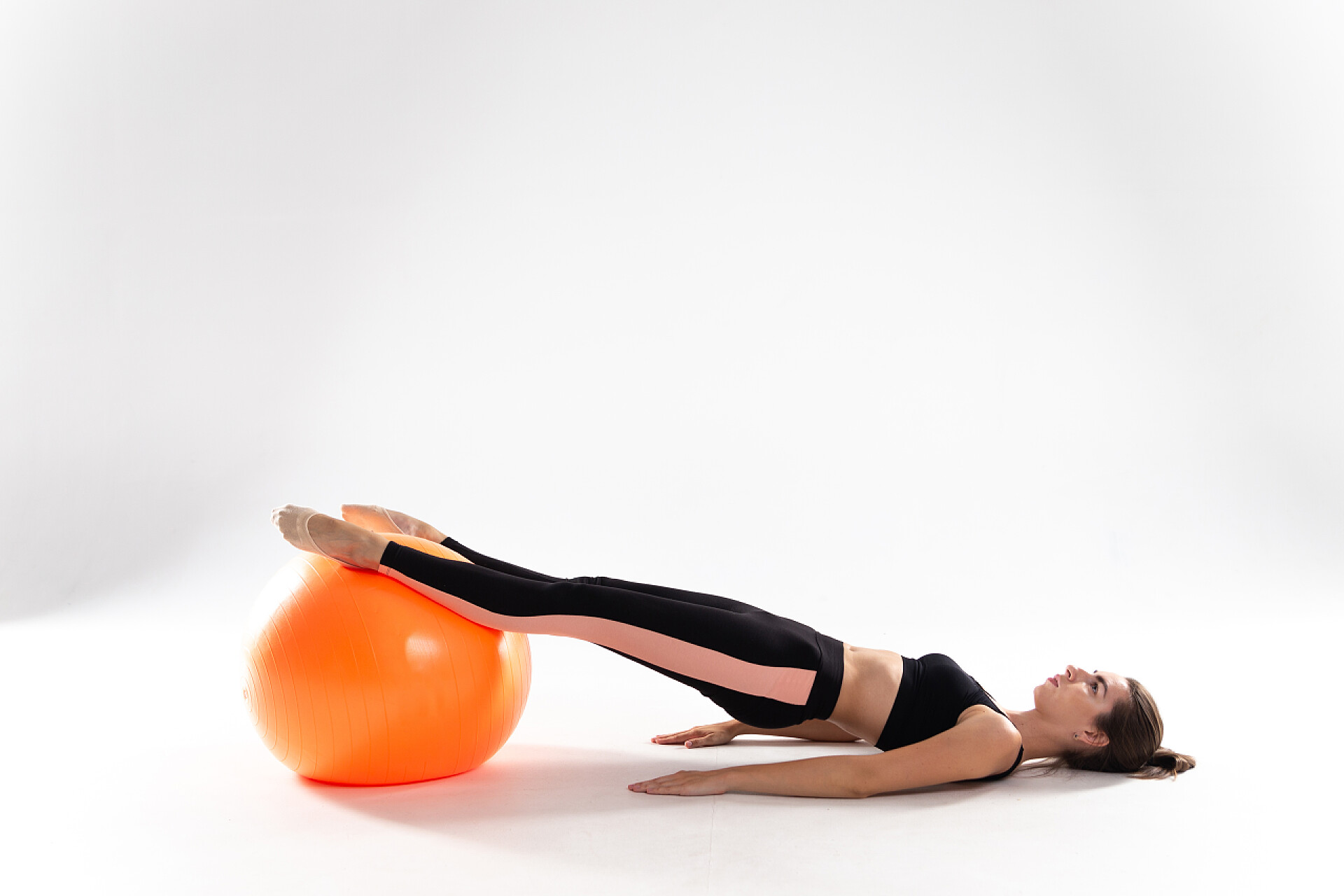 白色背景墙的女人在做瑜伽一个穿着腿和运动上衣的纤细女孩躺在一个白色孤立背景的健身球上。一个有着白色背景的女运动员，带着一个健身球.