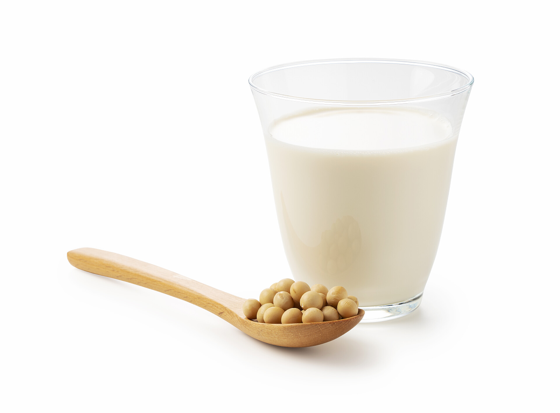 白色背景前的豆浆和黄豆将豆浆和大豆放入一个白色底座上的木制勺子的杯子中