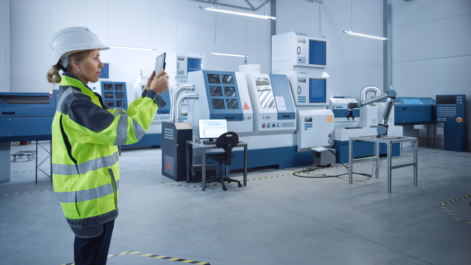 一个女工程师在用平板检查工厂所属行业4.0现代工厂：女工程师使用数码台式机与放大现实可视化车间制图、楼层布局。具有高科技数控机床和机器人臂的装置