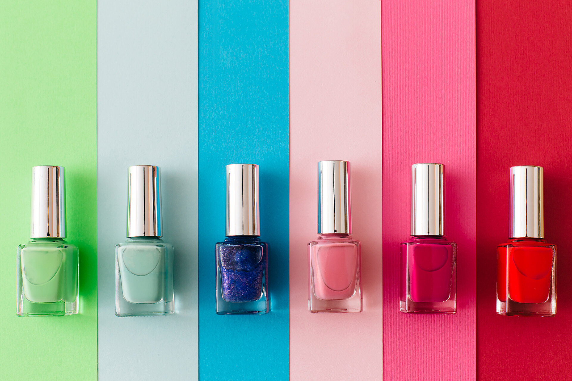 白色桌子上的指甲油一盒瓶瓶五颜六色的指甲油放在五颜六色的背景上.3.修指甲和修脚的概念。平面布局，顶视图，复制空间.