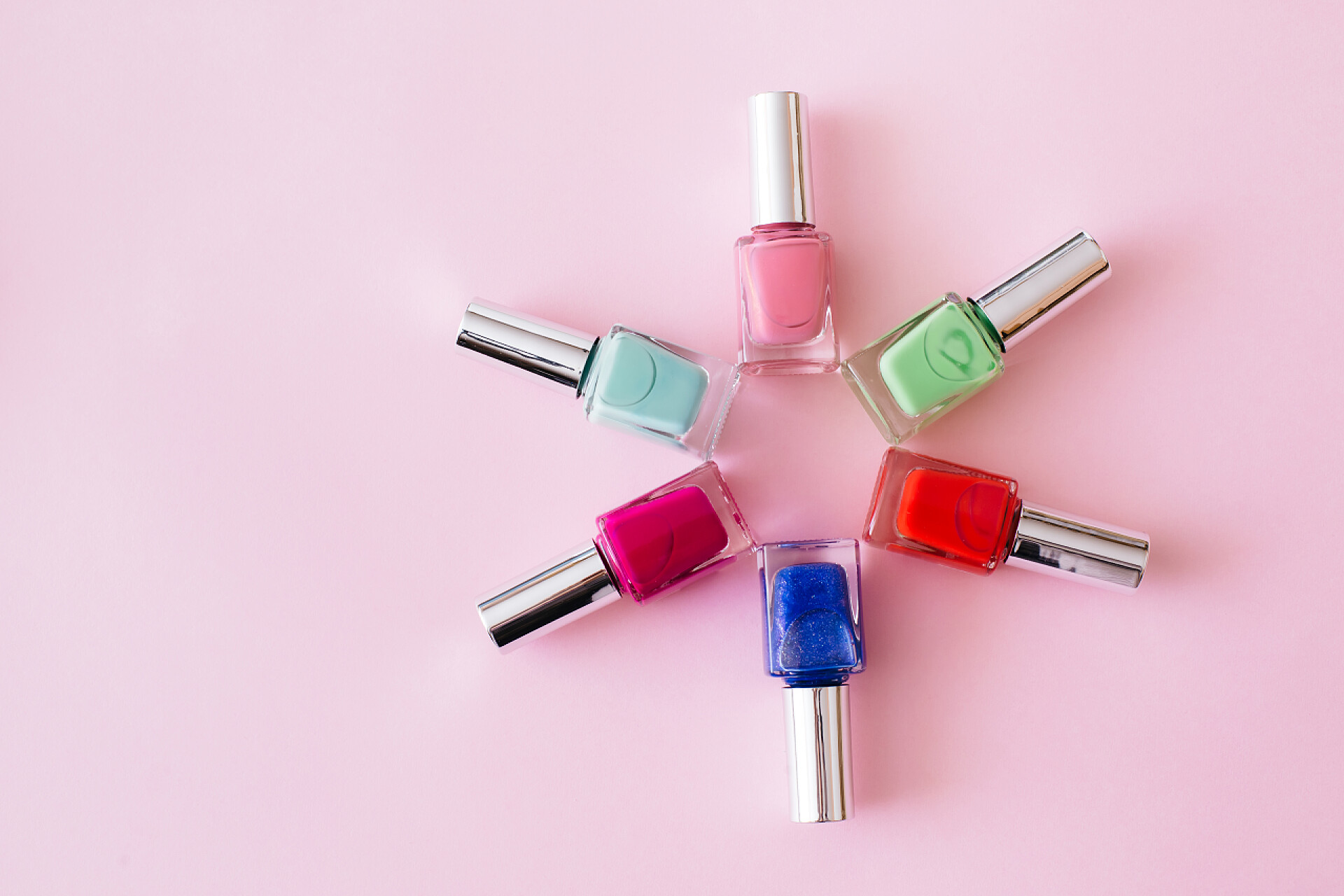 粉色桌子上的指甲油一盒瓶瓶五颜六色的指甲油涂在粉红的背景上.3.修指甲和修脚的概念。平面布局，顶视图，复制空间.