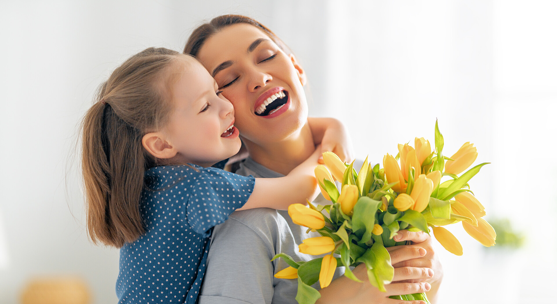 送给妈妈花朵的女儿抱着妈妈母亲节快乐。小女儿向妈妈表示祝贺,并送给她鲜花.妈妈和女孩笑着和拥抱。家庭假日和团聚.
