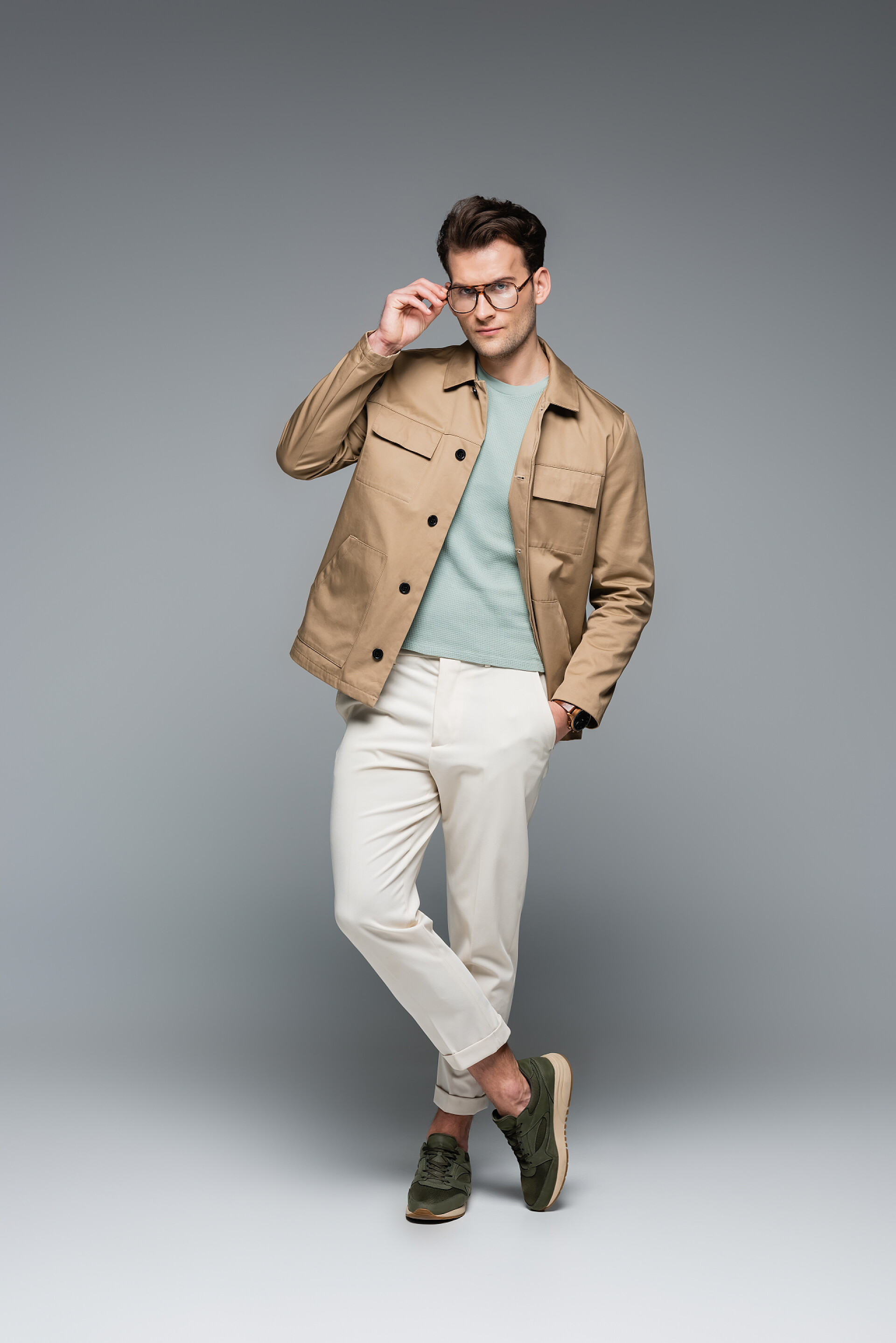 灰色背景下一个男人在拍照全身上下都是穿着时髦服装、手插灰色口袋的时髦男人