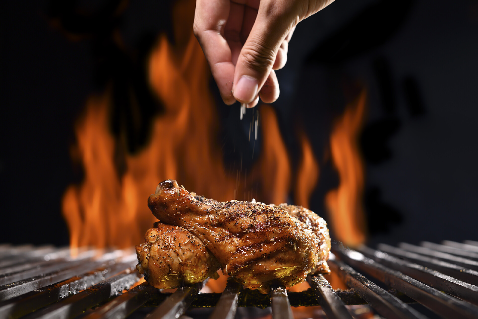 在烧烤架上烧烤的鸡腿在烤鸡腿上的火烤架上手工撒盐和调味品