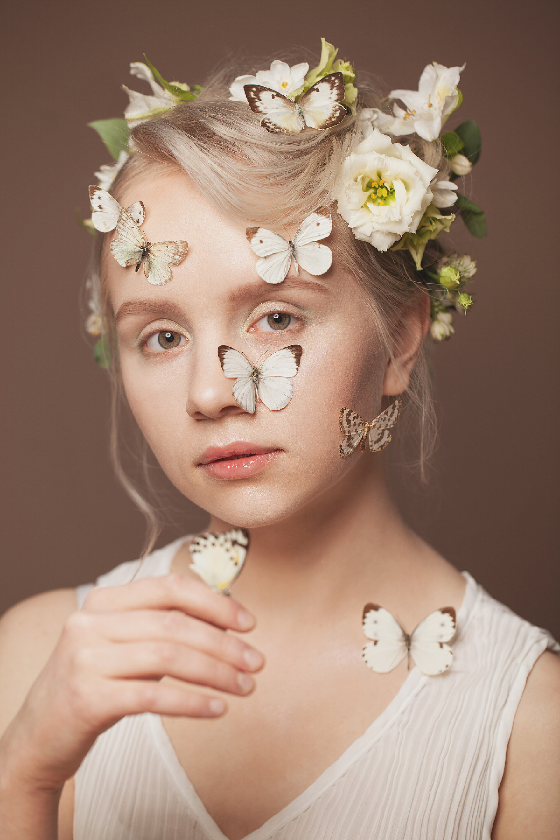 咖啡色背景前的女人俊俏的金发女模特的合影，有着健康的发型，春花洁白，背景为褐色，蝴蝶柔和