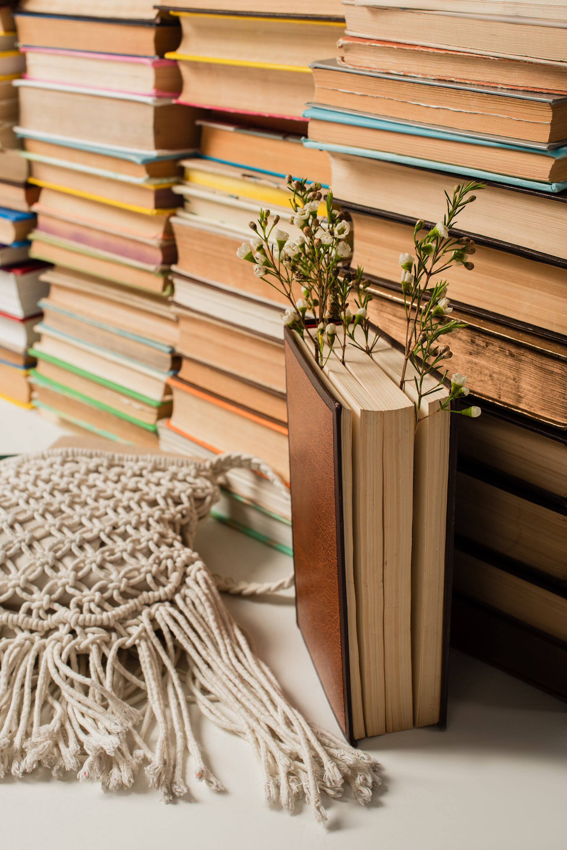 桌子上的书籍野花接近模糊的书堆，书堆上有精装书和白色的针织交叉装袋