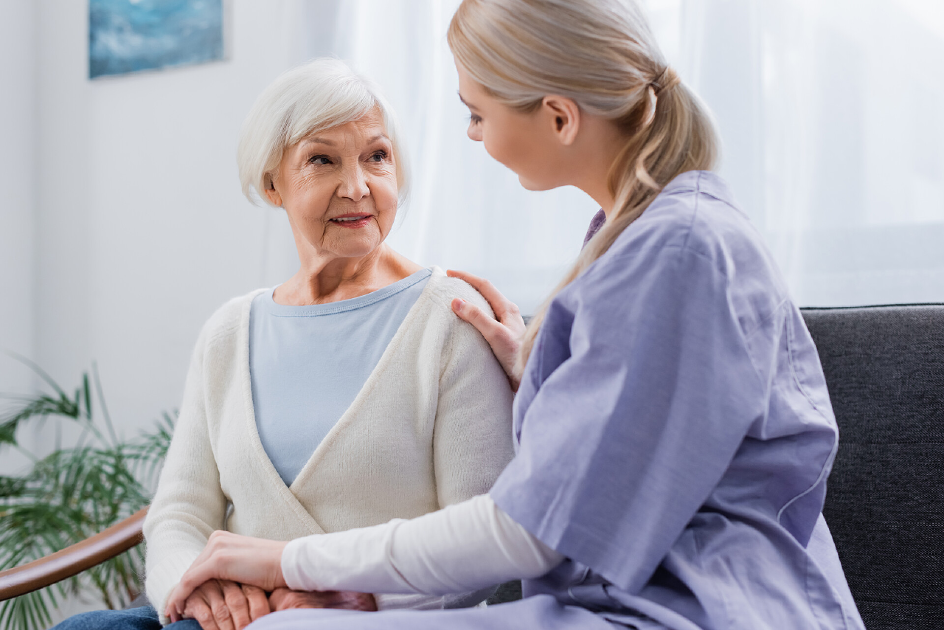 坐在沙发上的奶奶和护士社工在家中与年长妇女手牵手