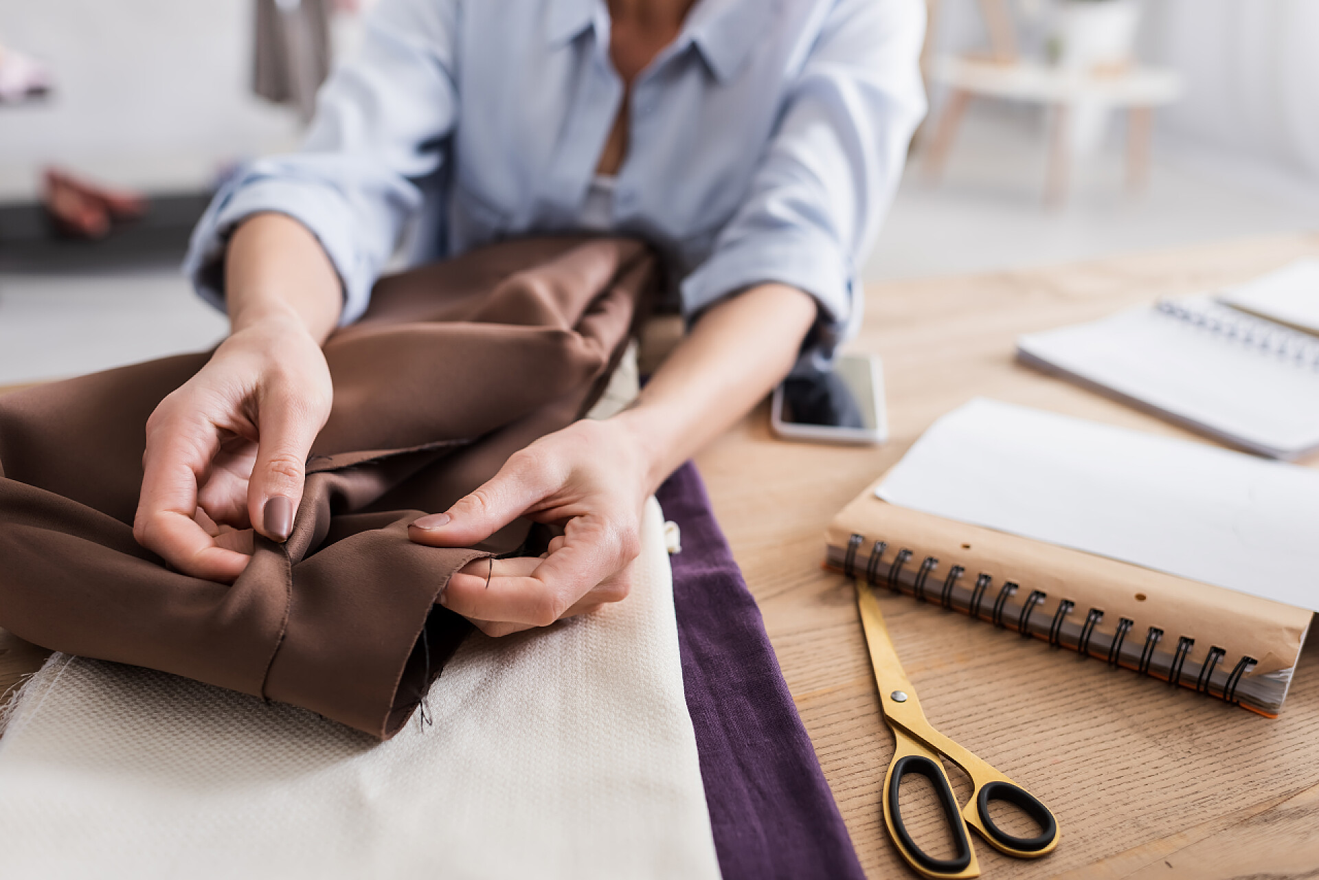一个女人拿着一大块布料模糊的设计师在剪子和笔记本附近拿着布的剪影 