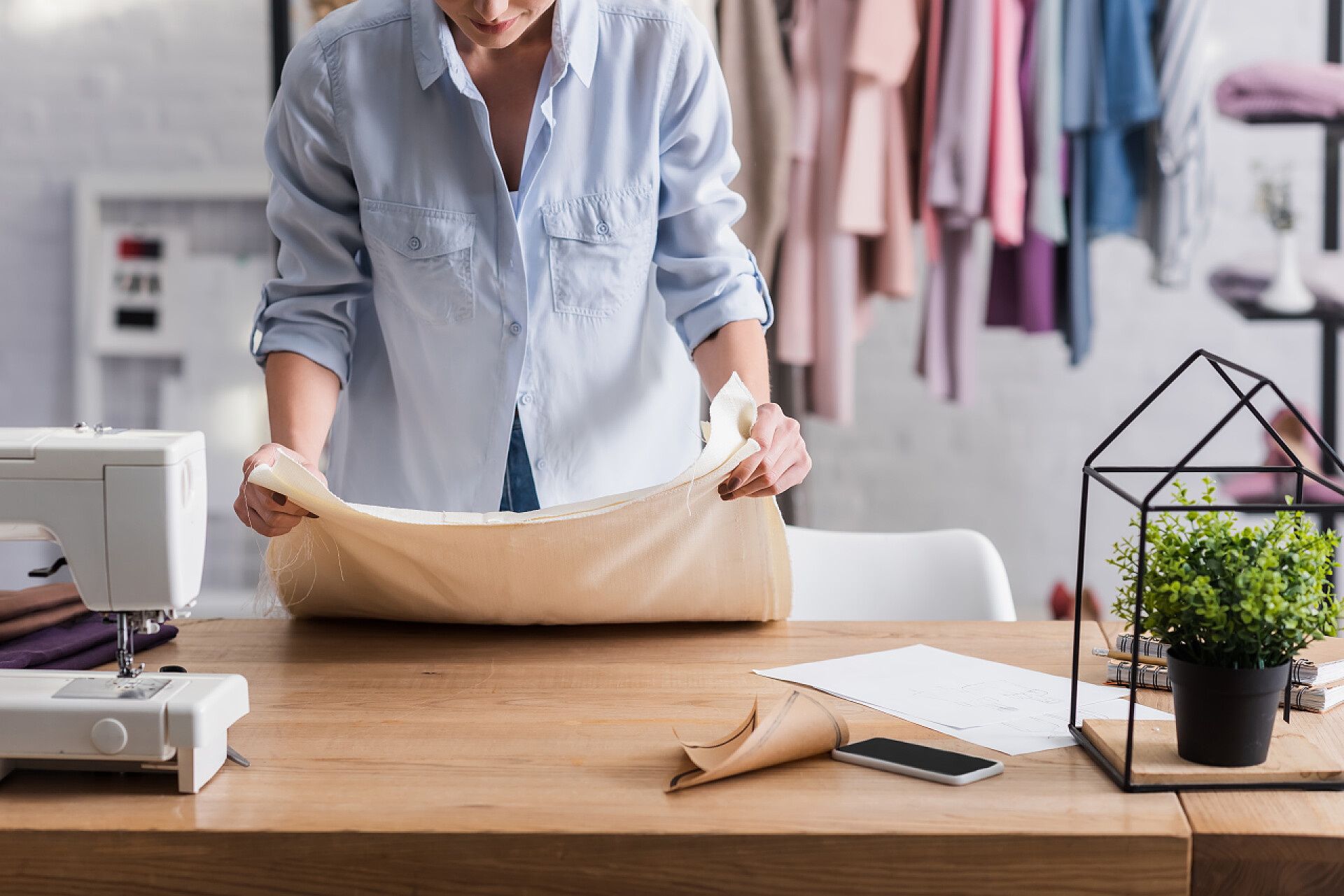 一个裁缝师在裁剪布料智能手机和缝纫机附近的裁缝师托布裁剪视图 