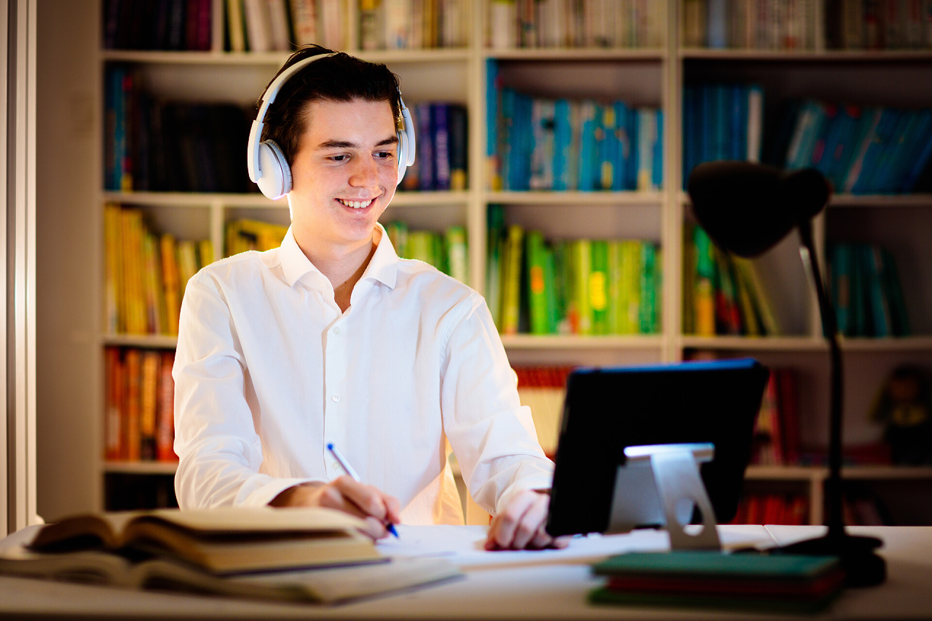 一个男人在挑灯学习在笔记本电脑的青少年学生。高中或大学的在线远程学习。有电话和平板电脑的青少年做作业和学习准备考试。在图书馆或教室里看书的年轻人.