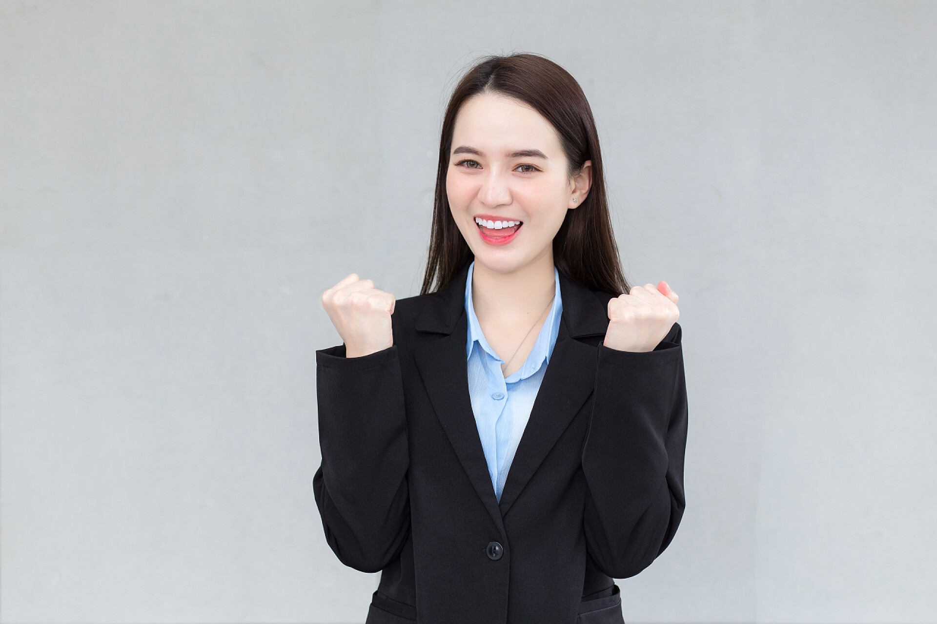 灰色背景前的一个美女身穿黑色西服的亚洲职业女性看上去很快乐，她笑得很开心.