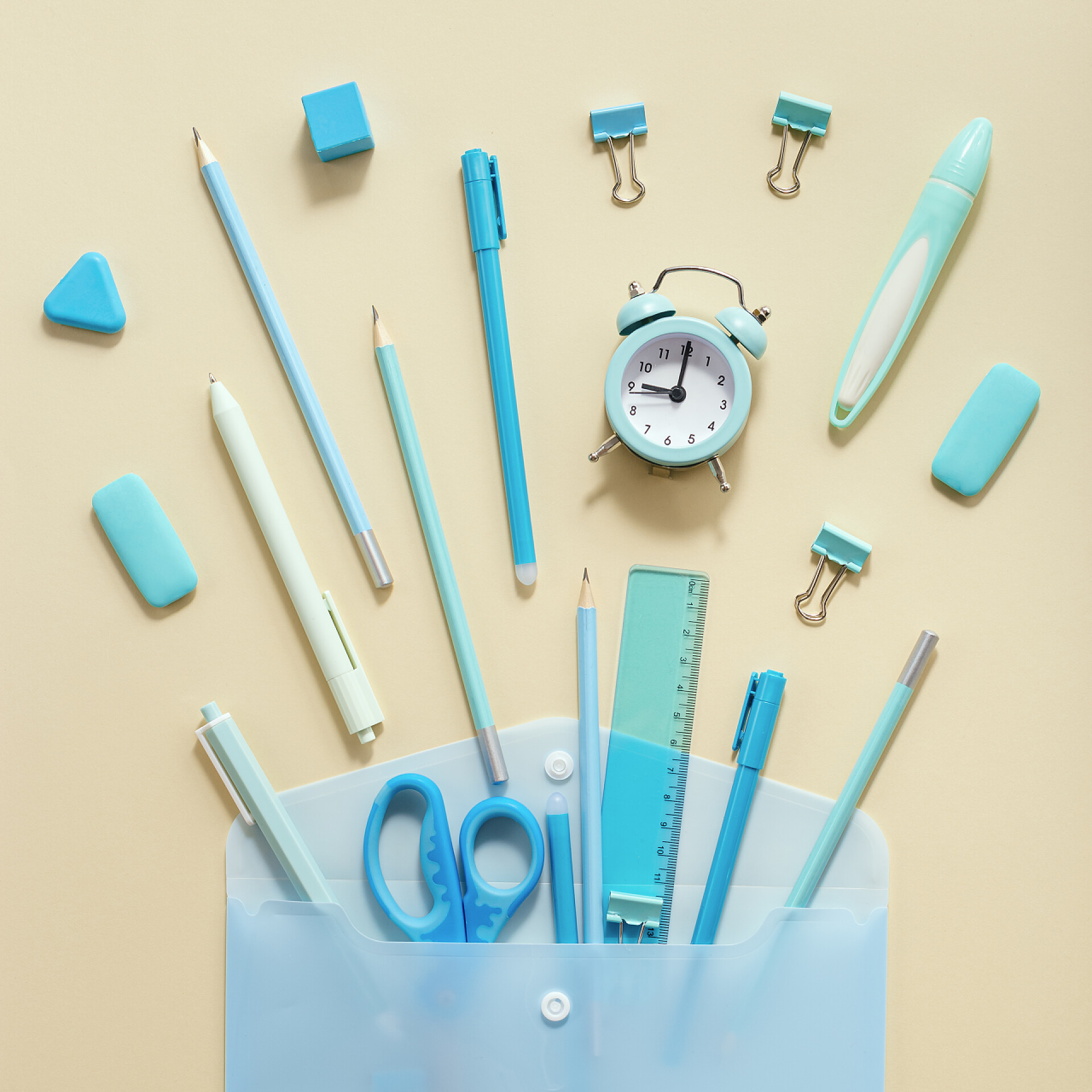 米色桌子上的文具用品回到学校创意的概念。打开信封，打开学习用品，铅笔，钢笔，尺子，浅黄背景的蓝色阴影.