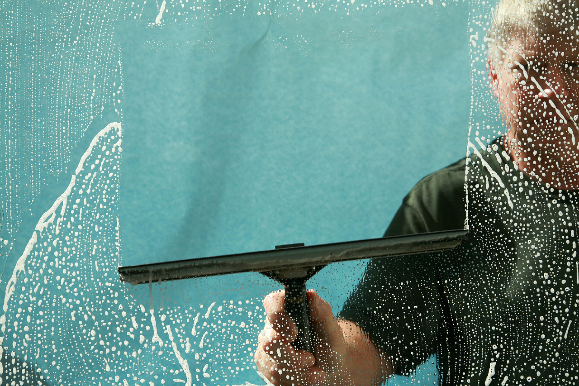 一个男人在用刷子在清理玻璃窗户清洁。洗窗。一个专业的窗户清洁剂肥皂和挤压窗户清洁剂。用刮胡刀擦窗户的清洁剂.办公室窗户清洁。办公室区的男工清洁玻璃墙。清洁服务. 