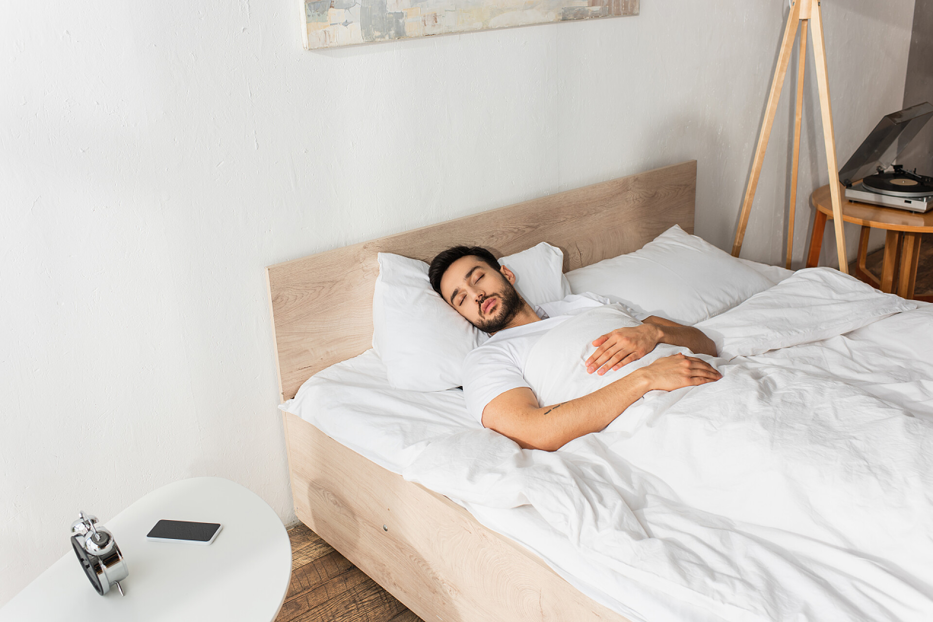 一个男人躺在床铺上睡觉3.睡在床头柜旁手机和闹钟旁边的年轻人 