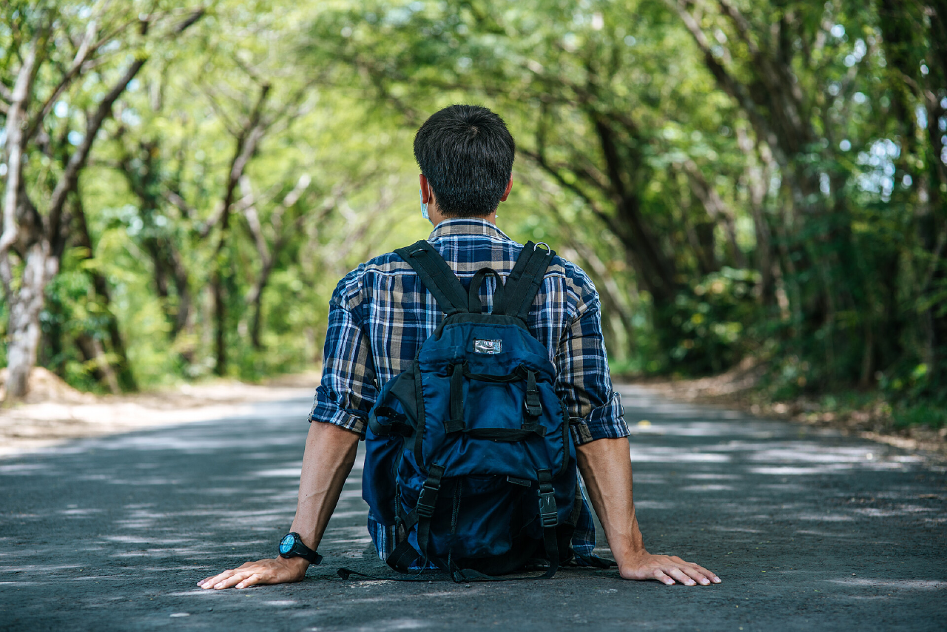 一个背着书包坐在地上的男人持面具、背着背包上路的男性游客.