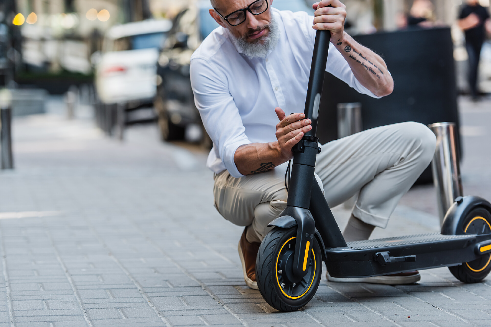 一个男人在修理滑板车mature man in glasses and shirt adjusting electric scooter on street 