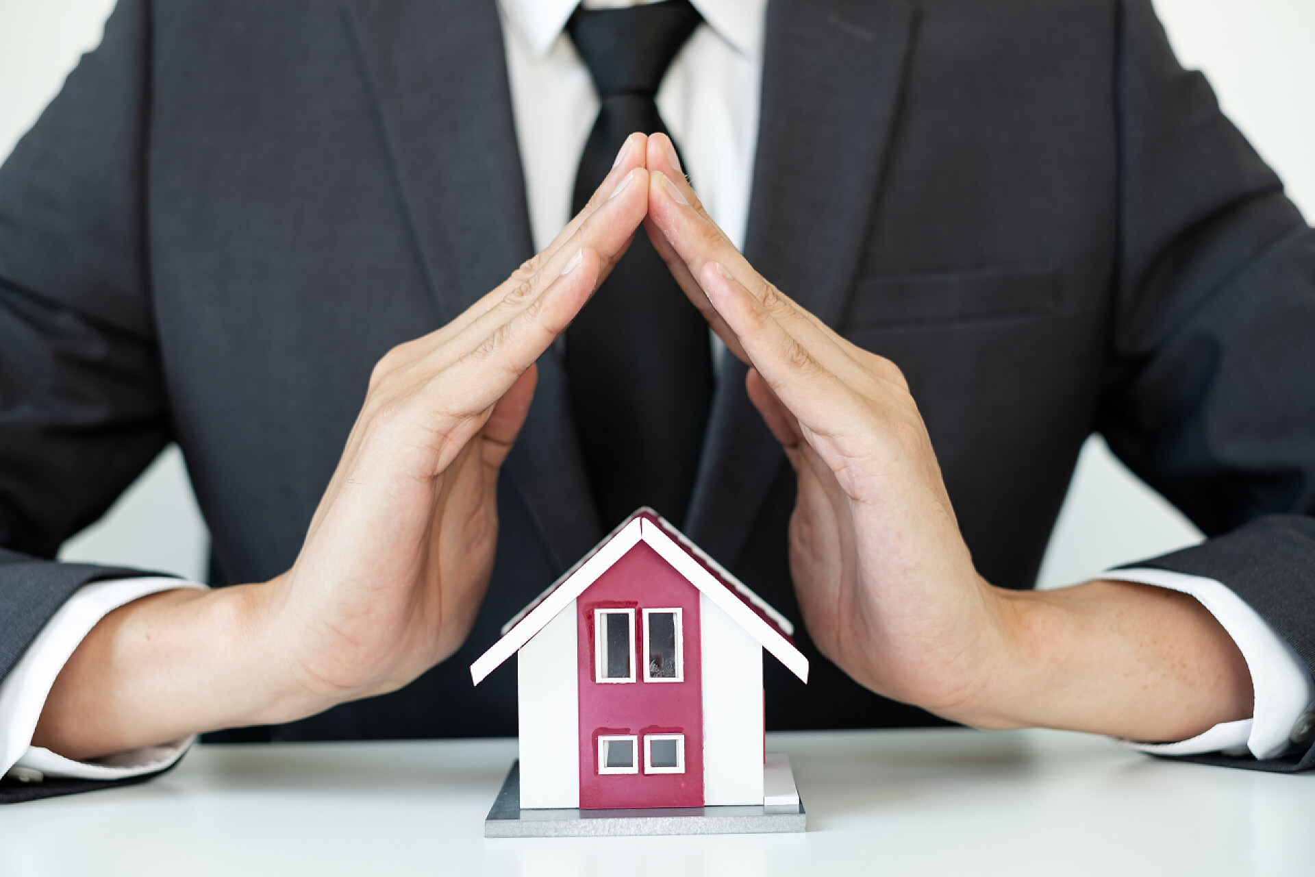 穿着西服的男人双手遮盖房顶房子由一名地产经纪人担保，为客户、购房者、保险者提供房屋保护，随时准备与新业主进行交易。房地产家庭保险概念.