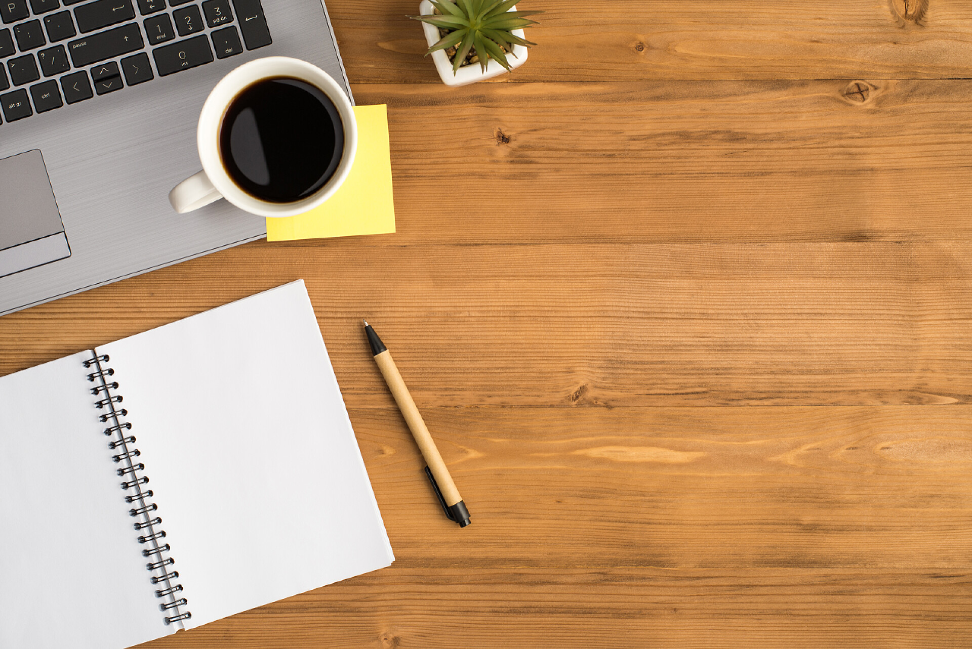 桌子上的笔记本电脑和笔记笔记本电脑花盆笔上的杯子黄色贴纸和隔离的木制桌子背景上空白开槽的俯瞰照片