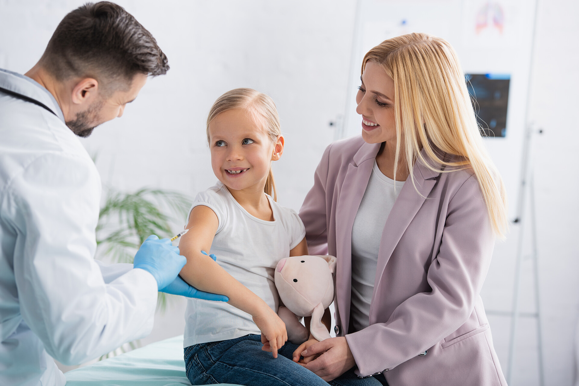 儿童保健在医院里接种疫苗的女孩在接种疫苗的过程中，带着注射器笑着看着医生身边的孩子 