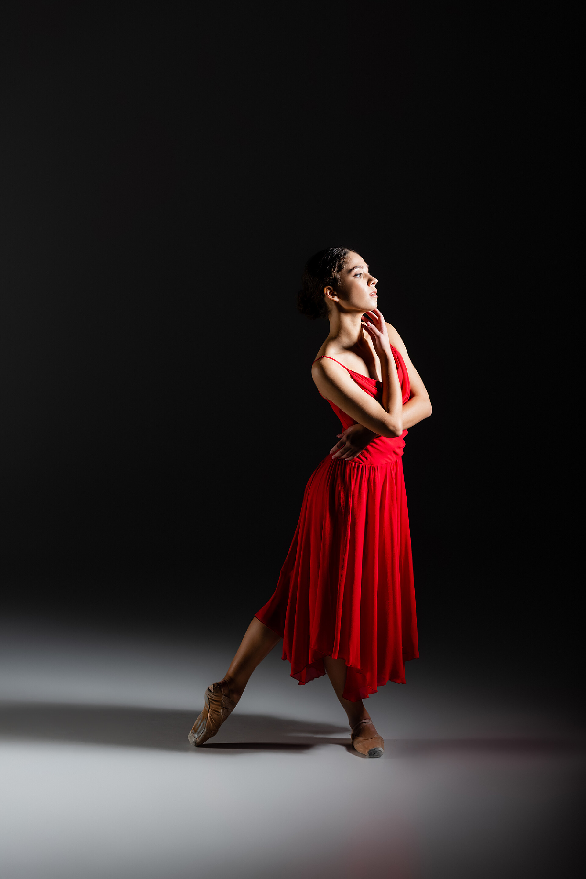 黑色背景墙，一个面向光源的女人穿着尖皮鞋站在黑色背景上的古典舞蹈演员侧视图