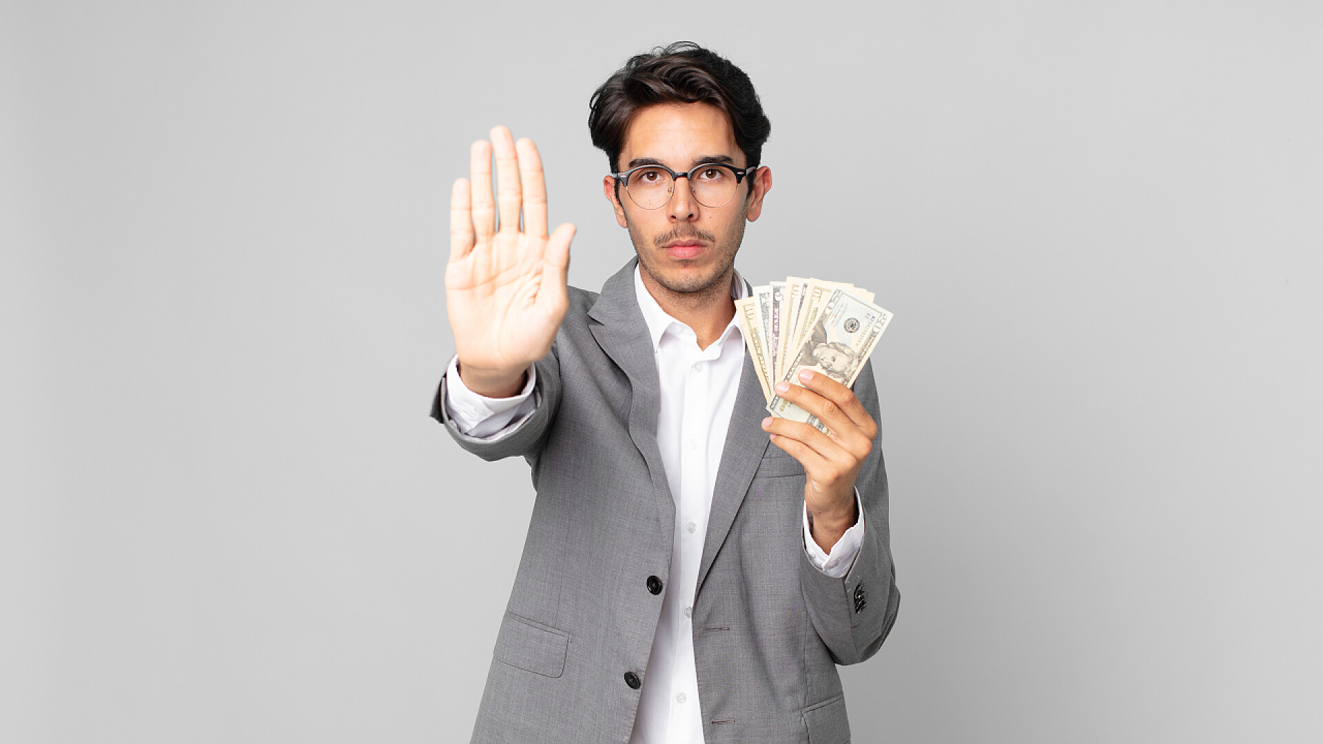 灰色背景前的一个男人对金钱说no年轻的惊慌失措的男人严肃地展示着张开的手心