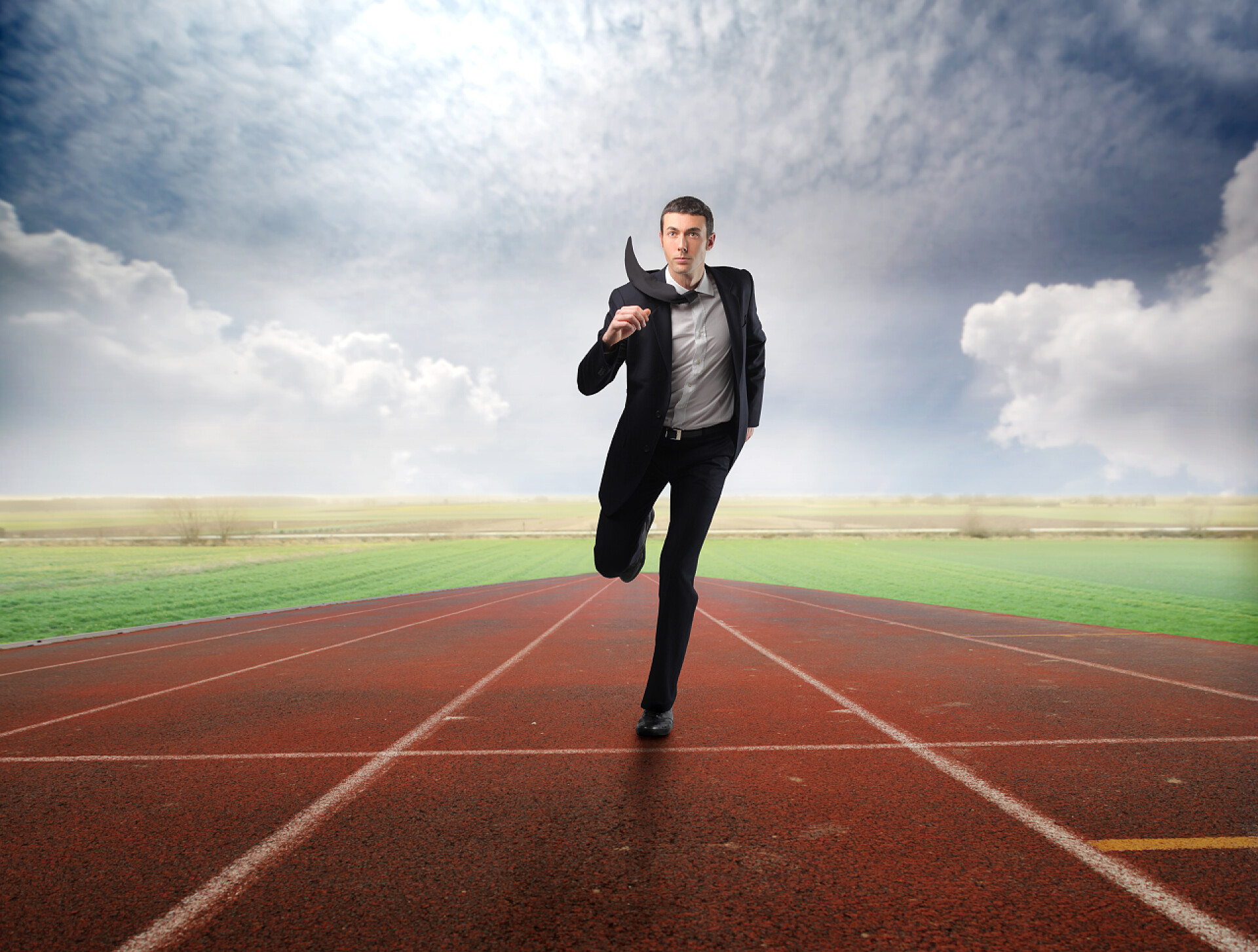 蓝天白云下在操场的跑道上奔跑的商务男士商务