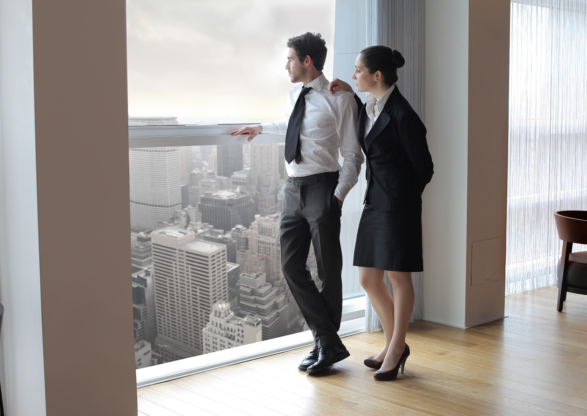 两个上班族在办公室的落地窗边向外看商务人士