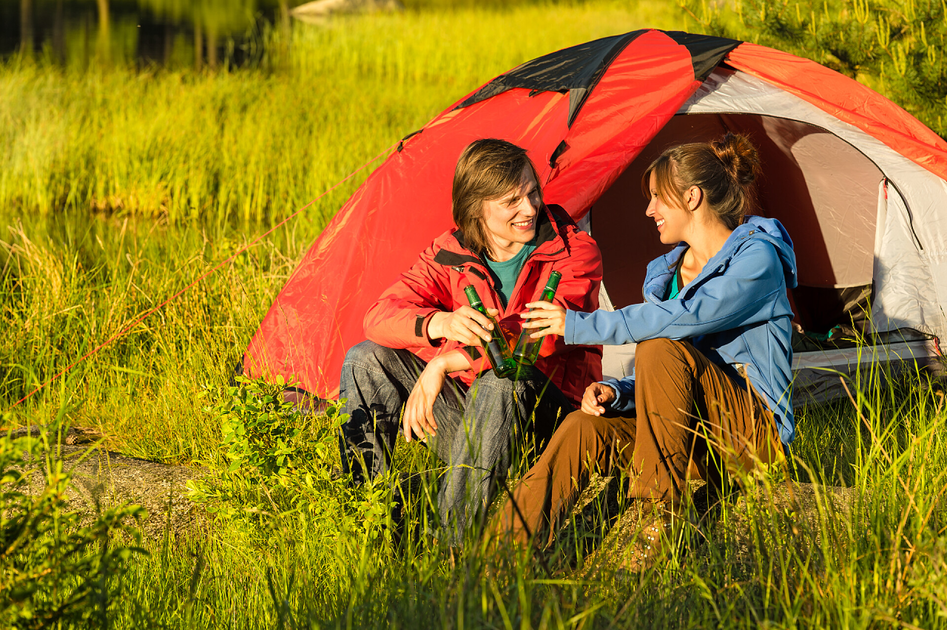 夕阳下露营的一对青年在草地上喝啤酒