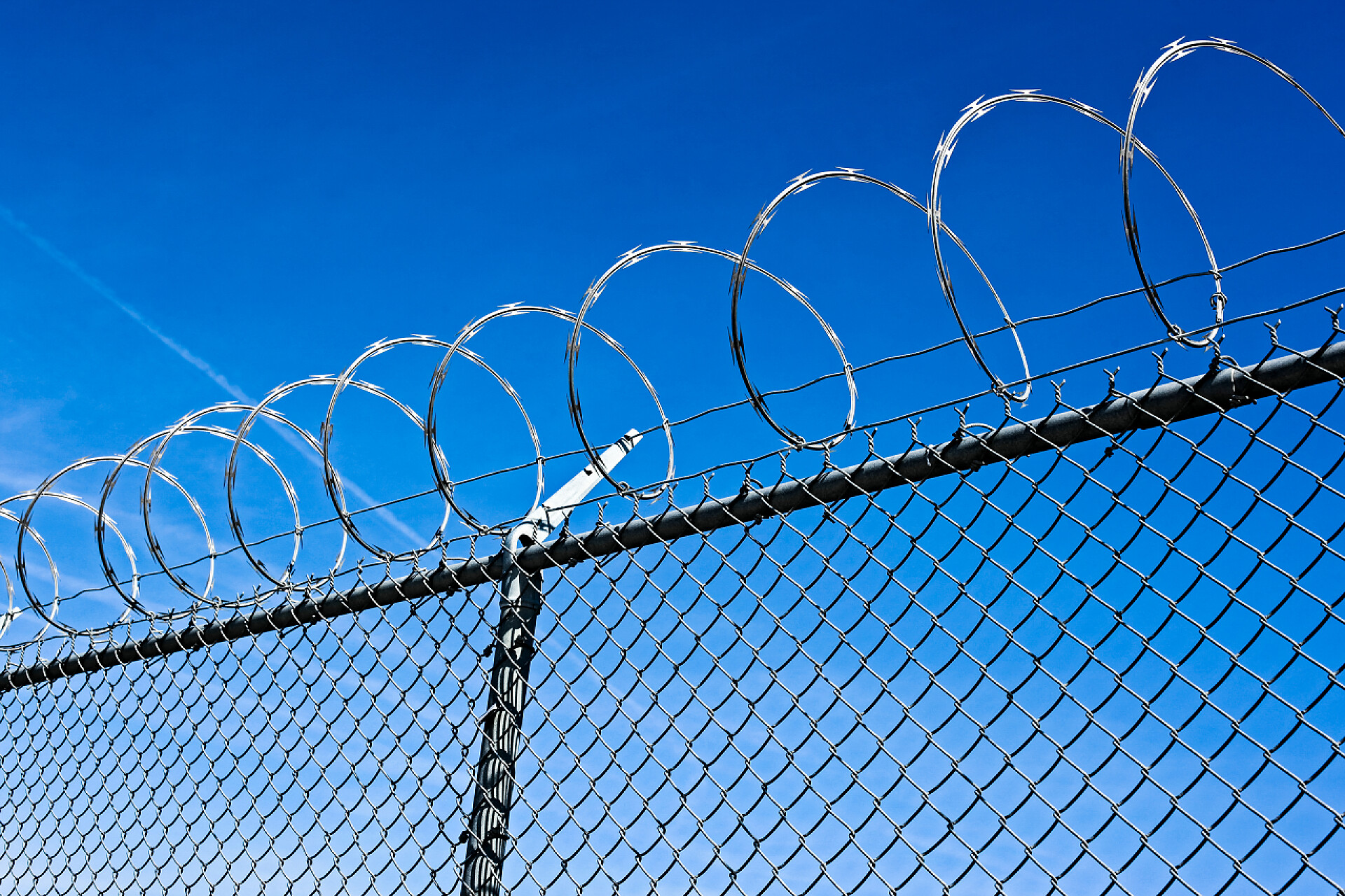 蓝色天空下金属栅有带刺的铁丝网安全防护