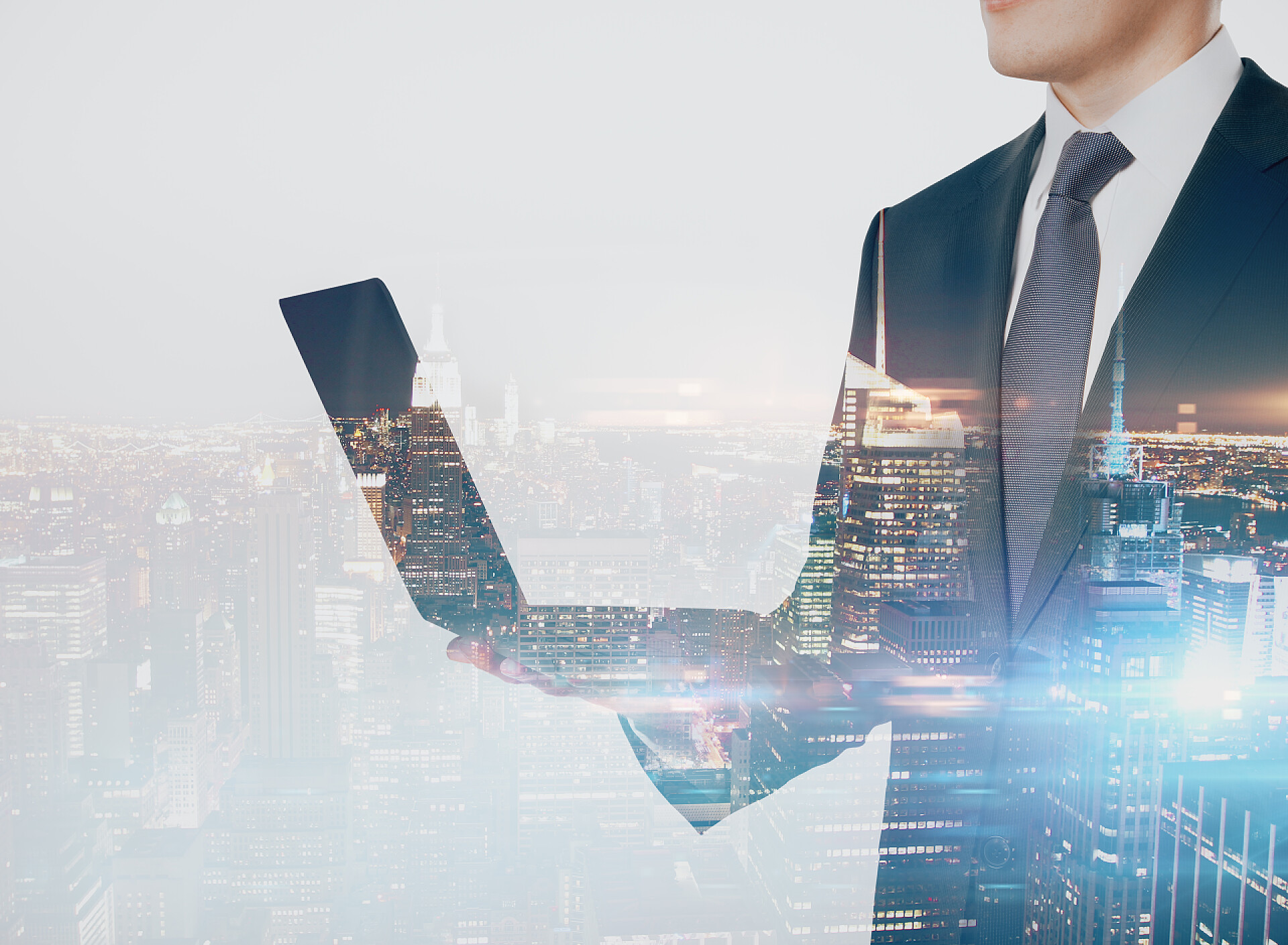 商务男白领站在写字楼里拿着笔记本电脑与繁荣城市夜景融合