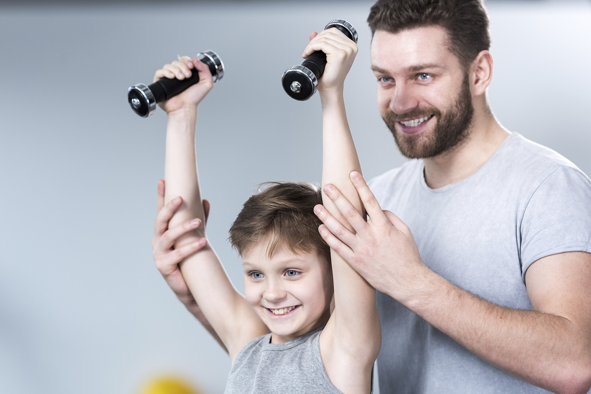 一个父亲在辅助男孩举着哑铃体育运动锻炼