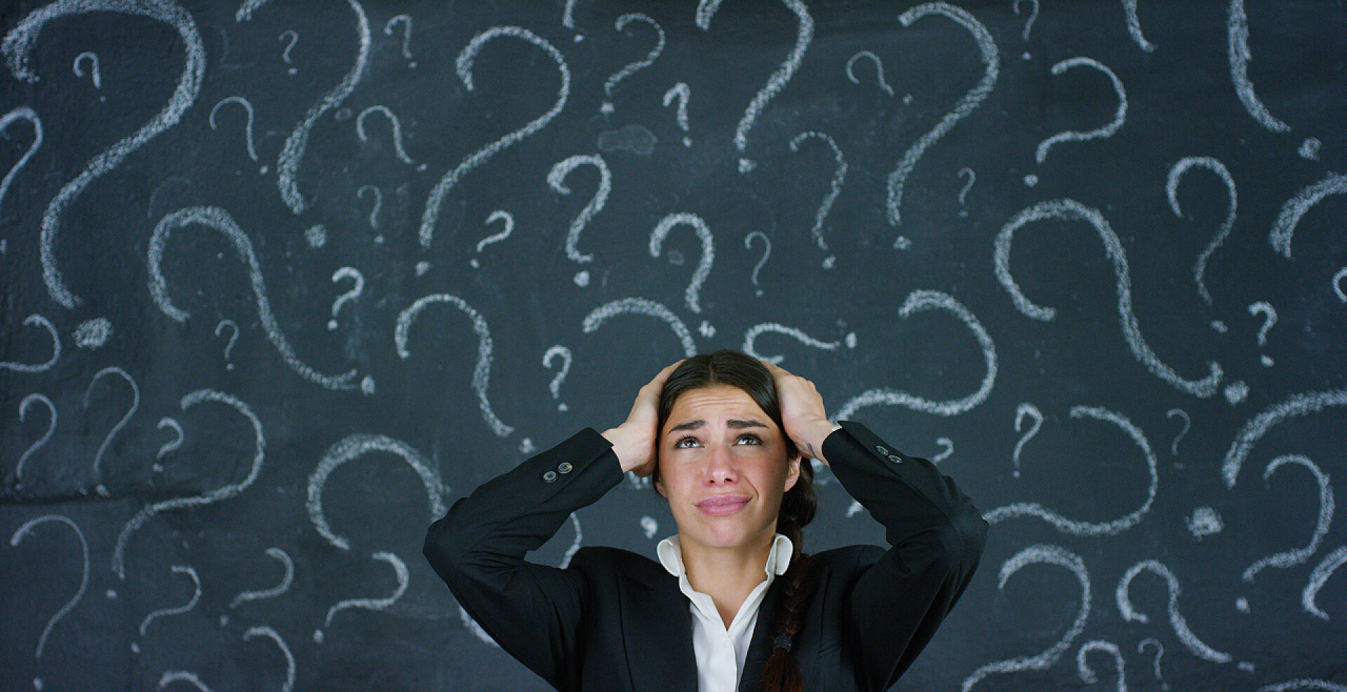 一个女人在打着问号的黑板背景上抚摸着脑袋问题困惑