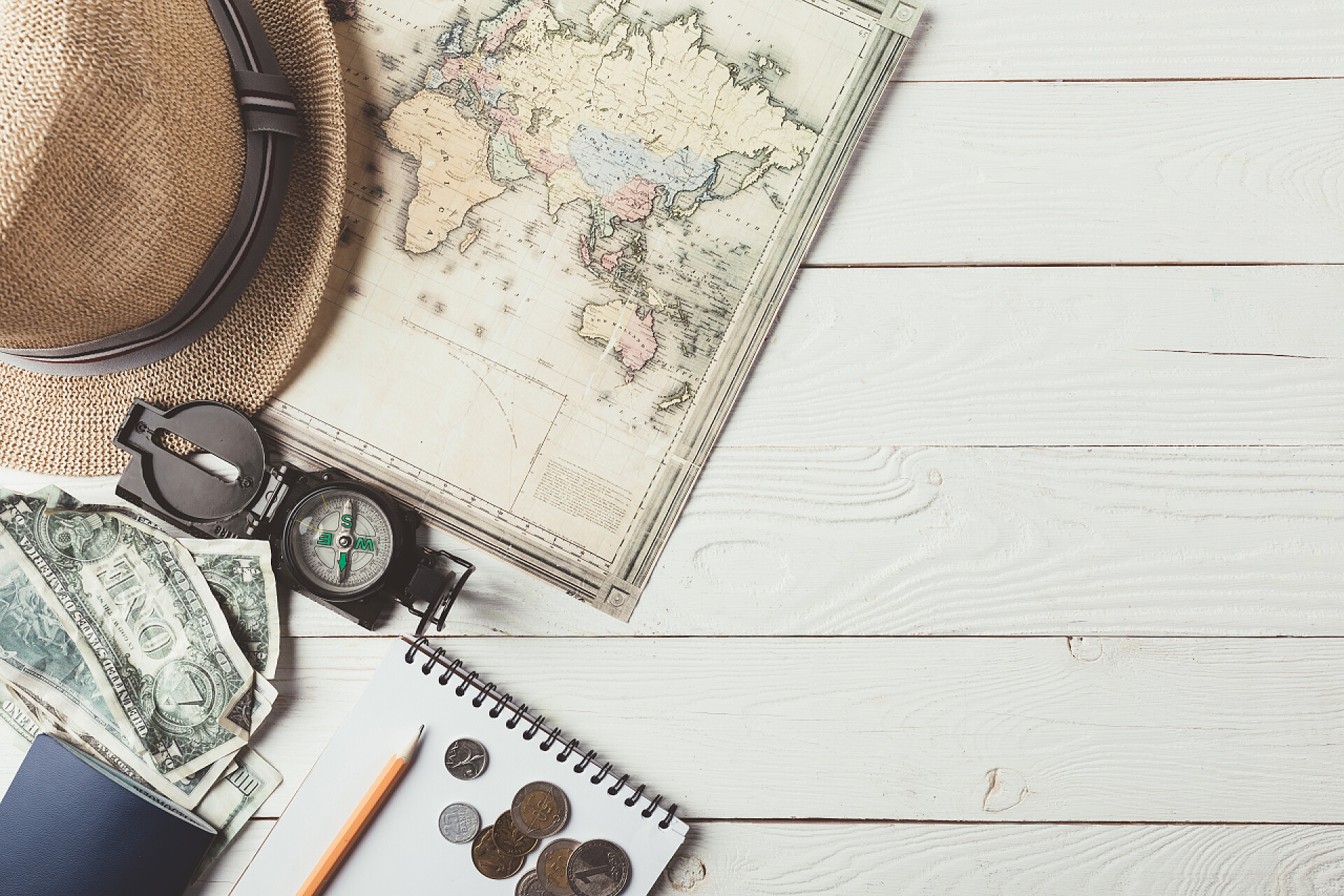 白色的木桌上摆放旅行用的罗盘帽子地图和钱币顶视图