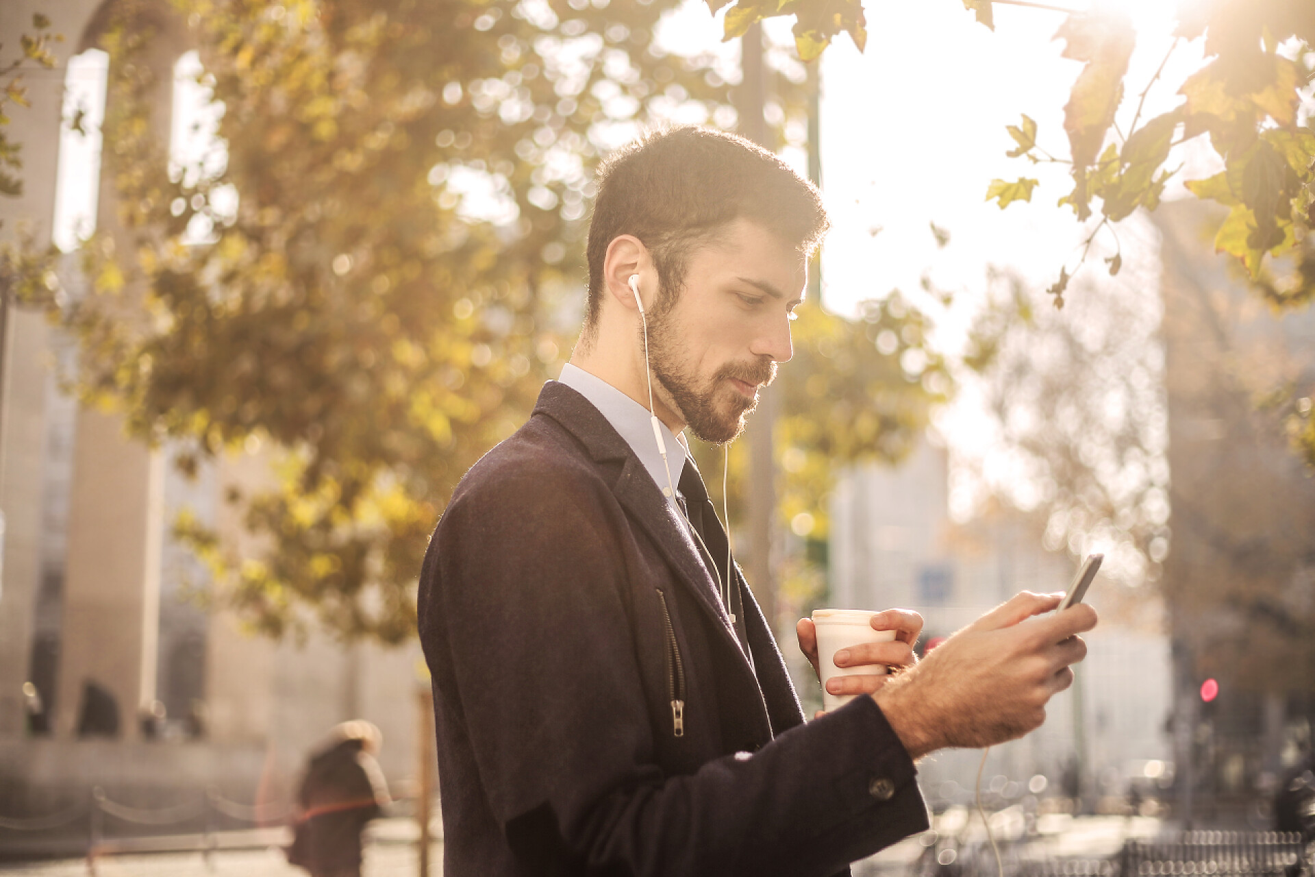 年轻的商人戴着耳机手拿咖啡和低头看他的智能手机上班族
