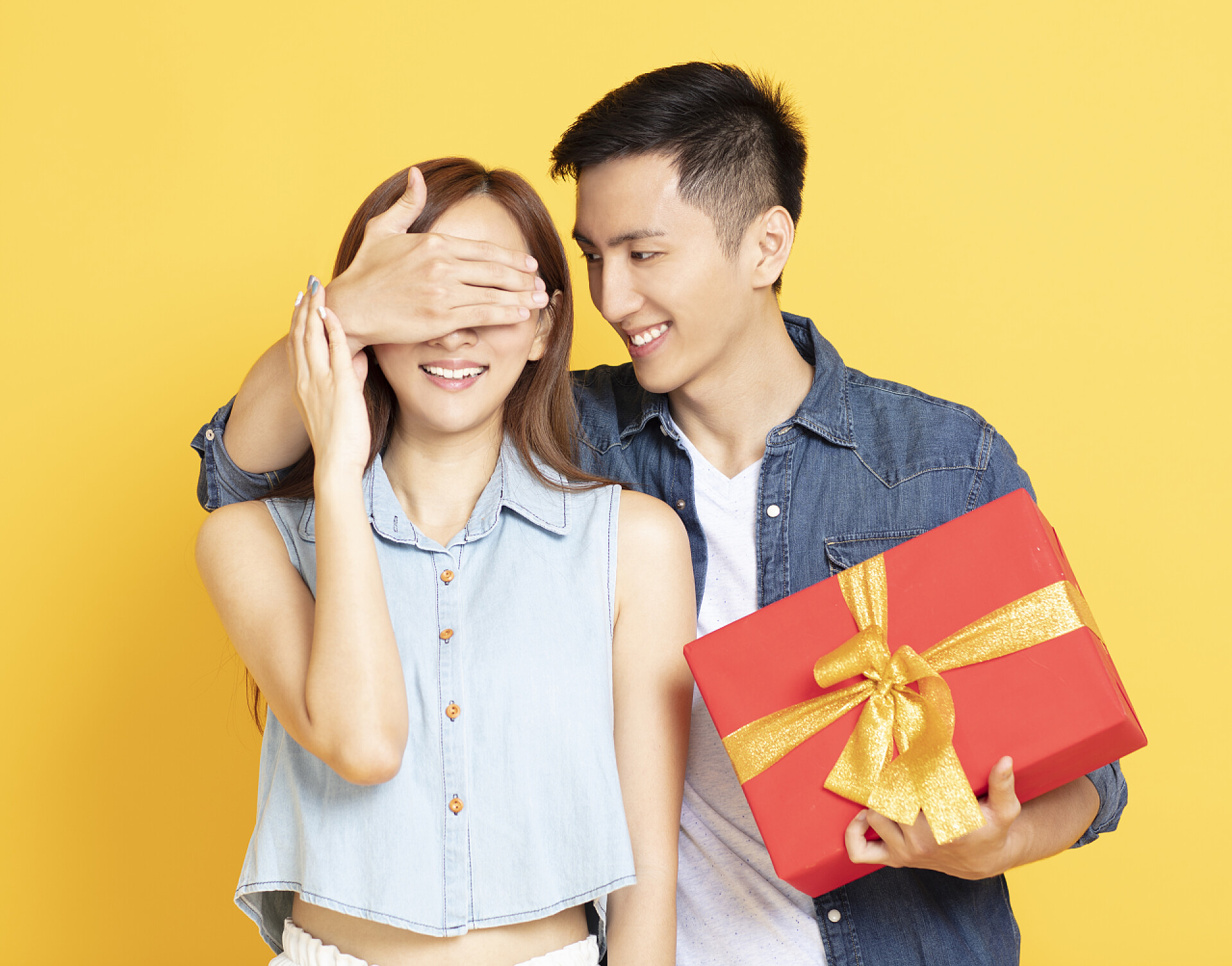 黄色背景中男人捂住女人的眼睛送礼物节日庆祝