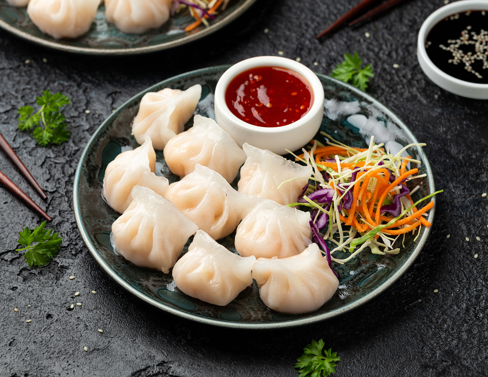 石桌上的一盘虾饺和配菜酱料食物、哈考或哈尔谷类。配菜、胡萝卜沙拉、大豆和甜辣椒酱.