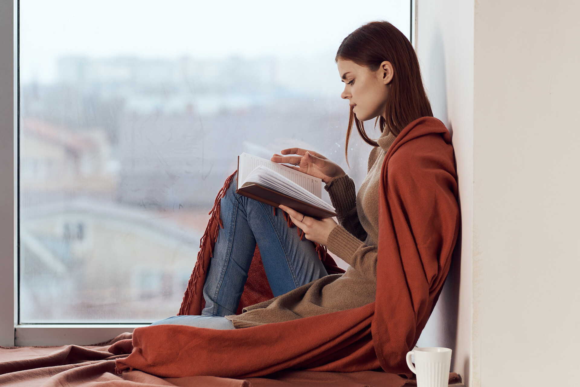 在窗台上看书的女人，喝了一杯热饮。高质量的照片