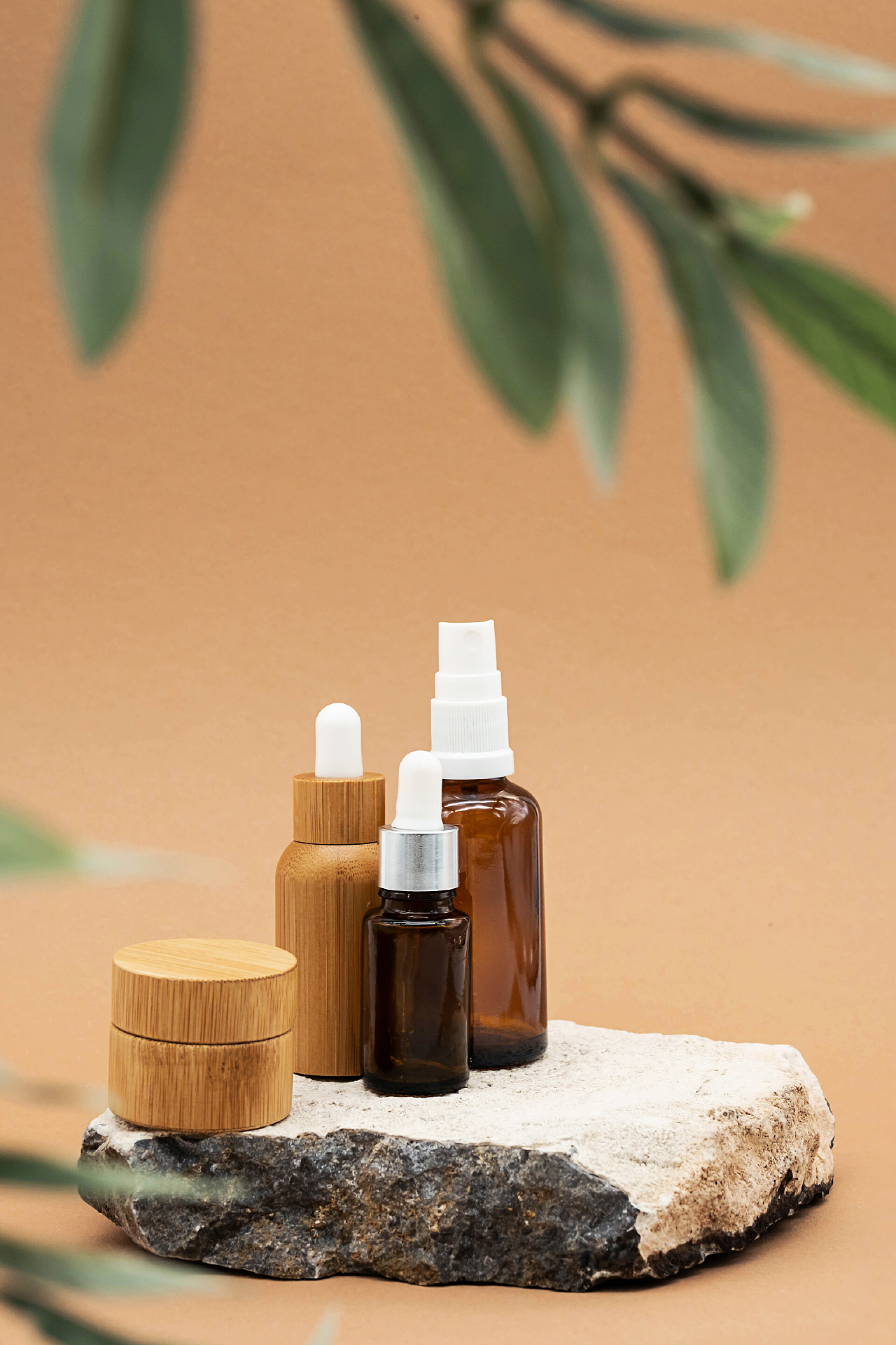 在模糊绿叶淡橙色背景下的琥珀色玻璃瓶和竹制精油瓶化妆品美容品模型化妆品美肤美妆
