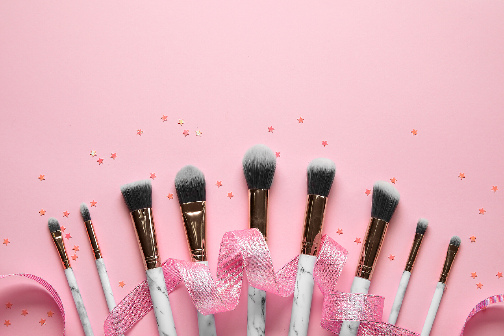 在粉色背景上的一套化妆刷和粉色彩带装饰