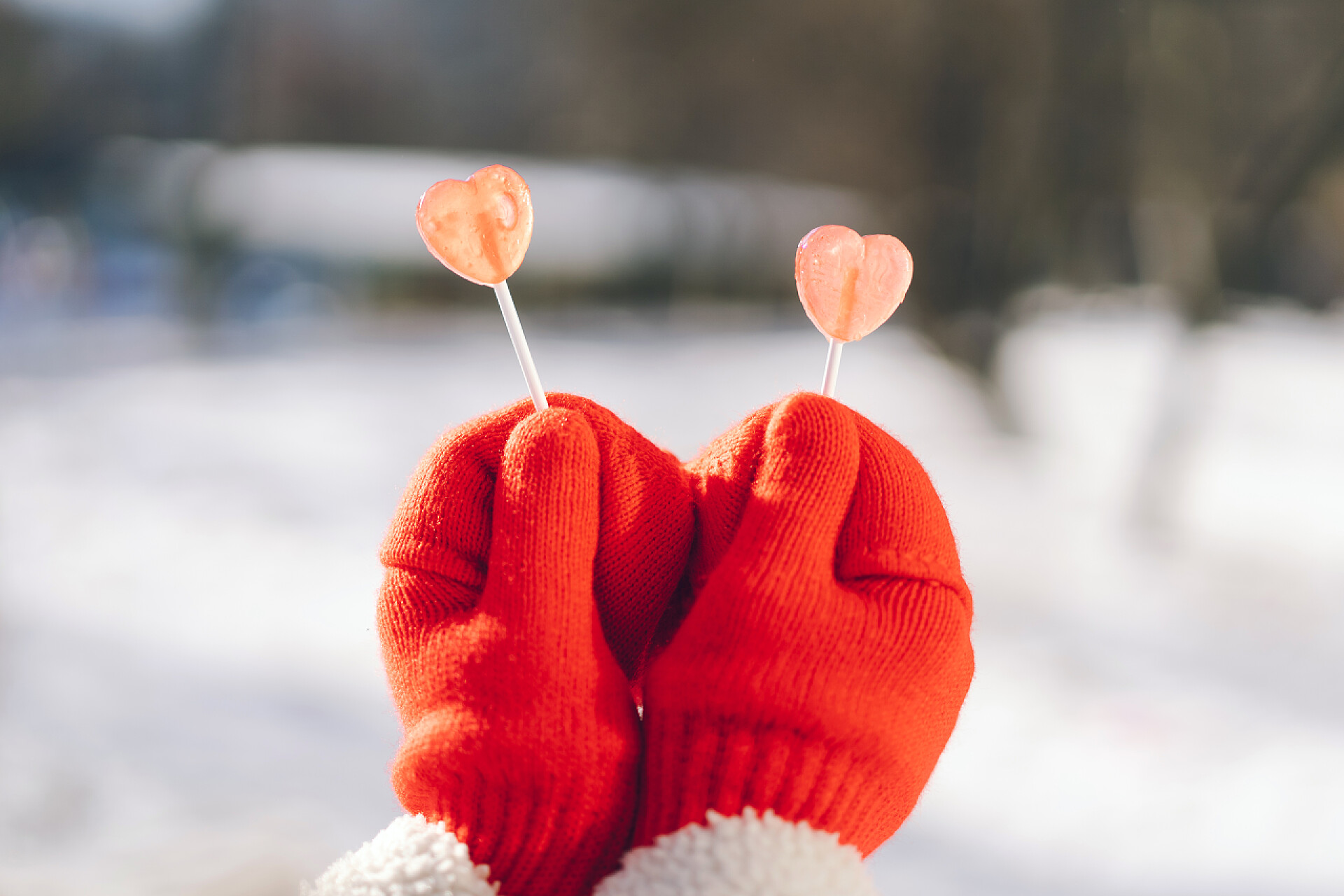 在冬天的模糊街道上戴红手套的双手拿着两片心形棒棒糖情人节