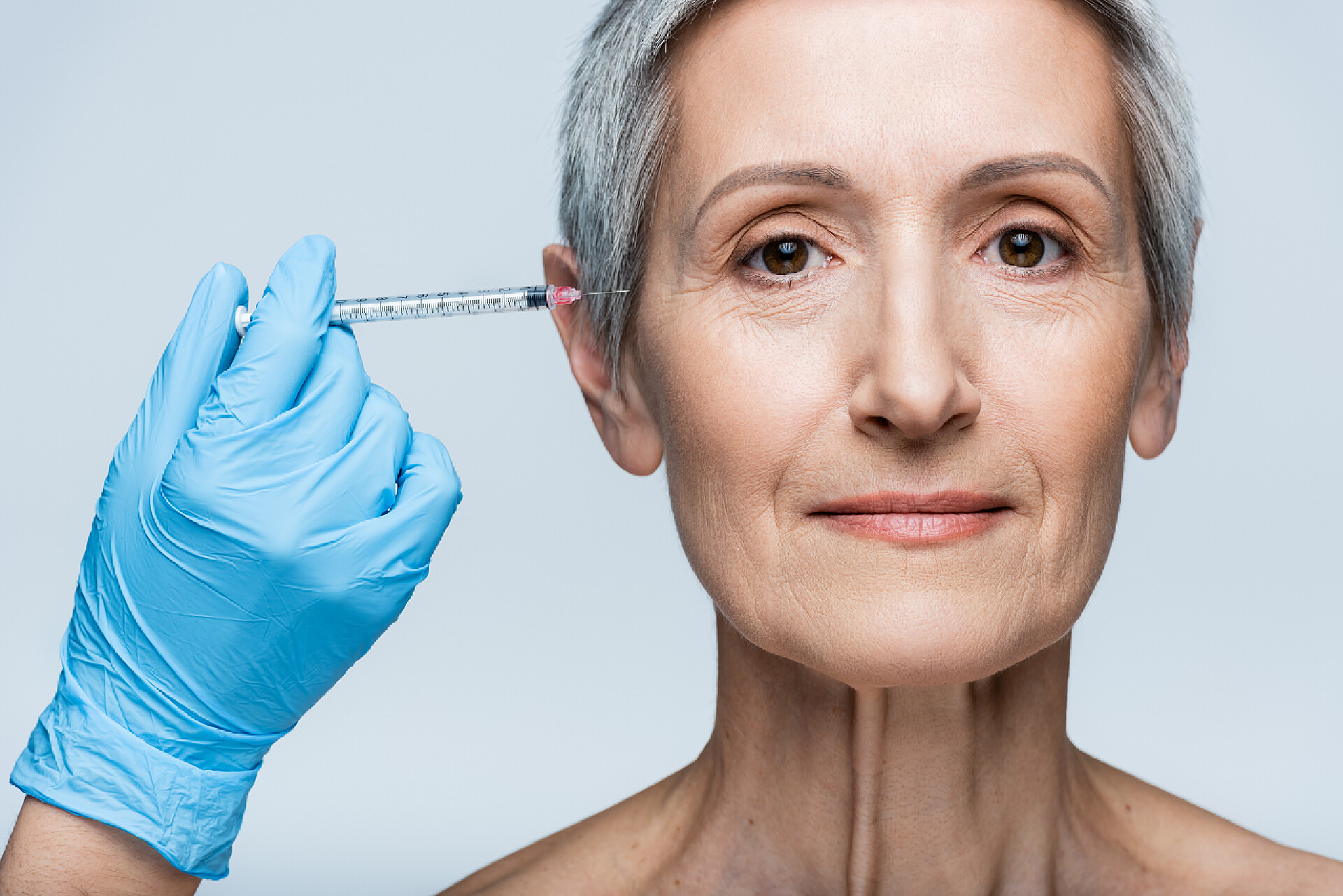医疗美容戴着乳胶手套的美容师拿着注射器给中年患者注射美容品