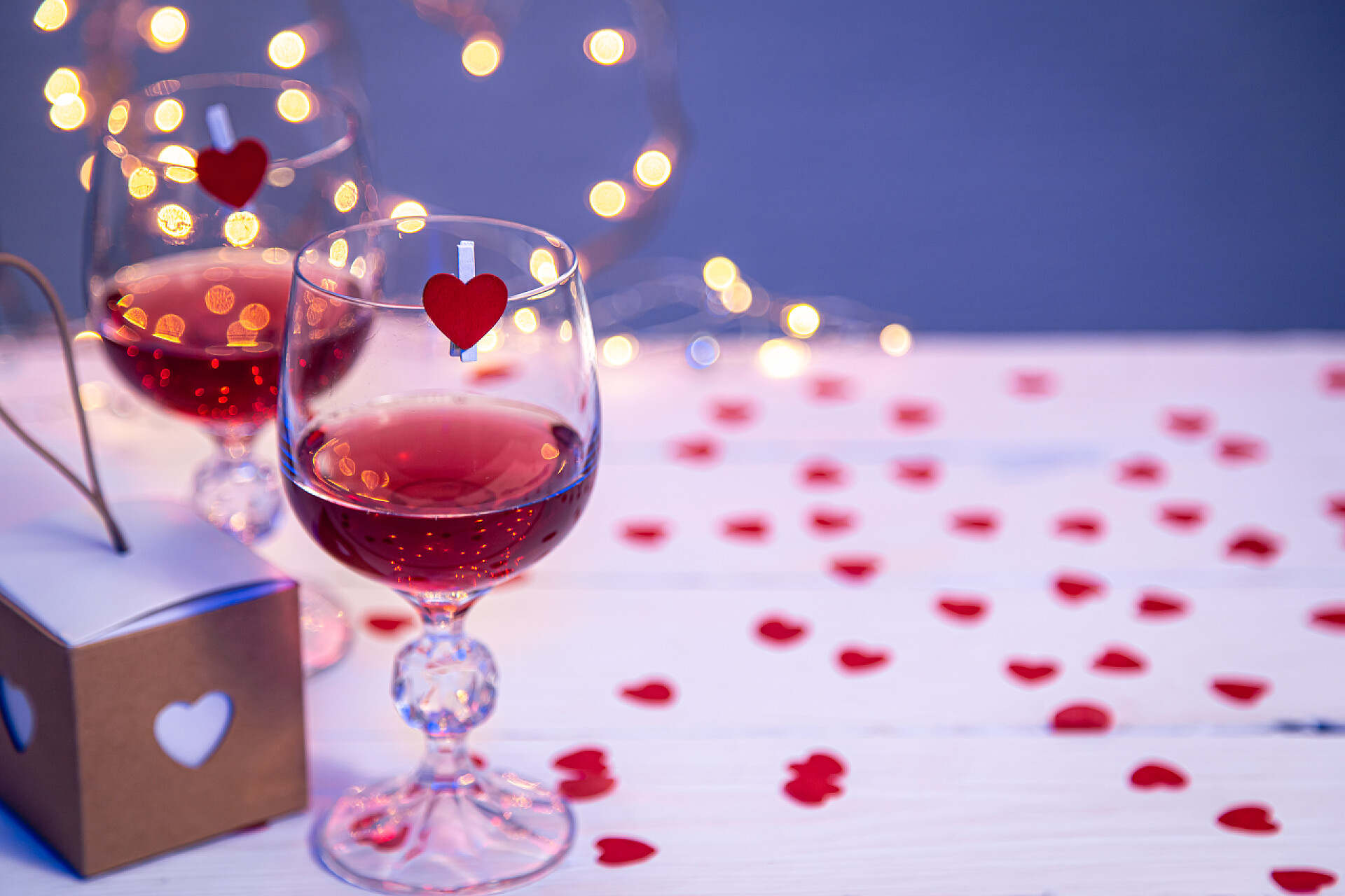 摆放粘着红色小爱心桌子上的两杯红酒烛光晚餐